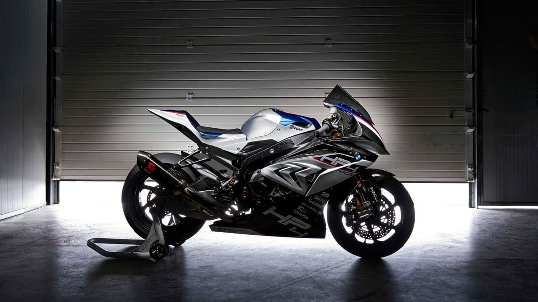 BMW HP4 Race motorcycle with carbon fiber frame and Akrapovič exhaust in a backlit garage setting.