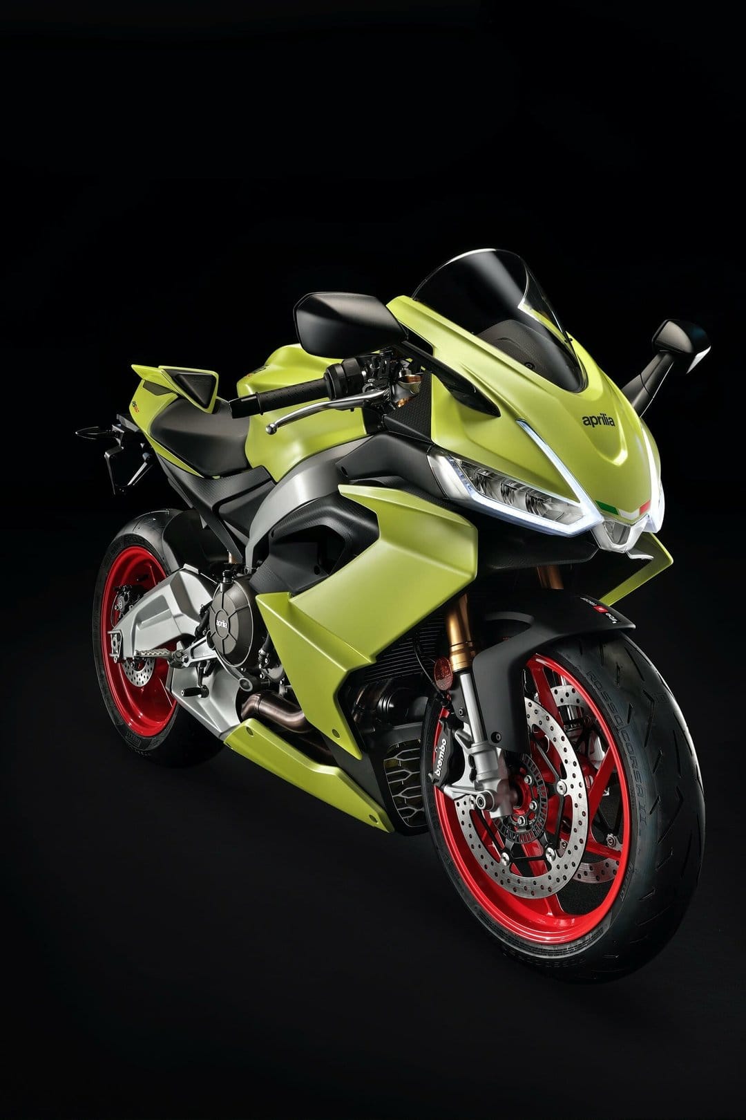 Aprilia RS 660 sportbike in Acid Gold with red wheels and glowing LED headlights on a black background.