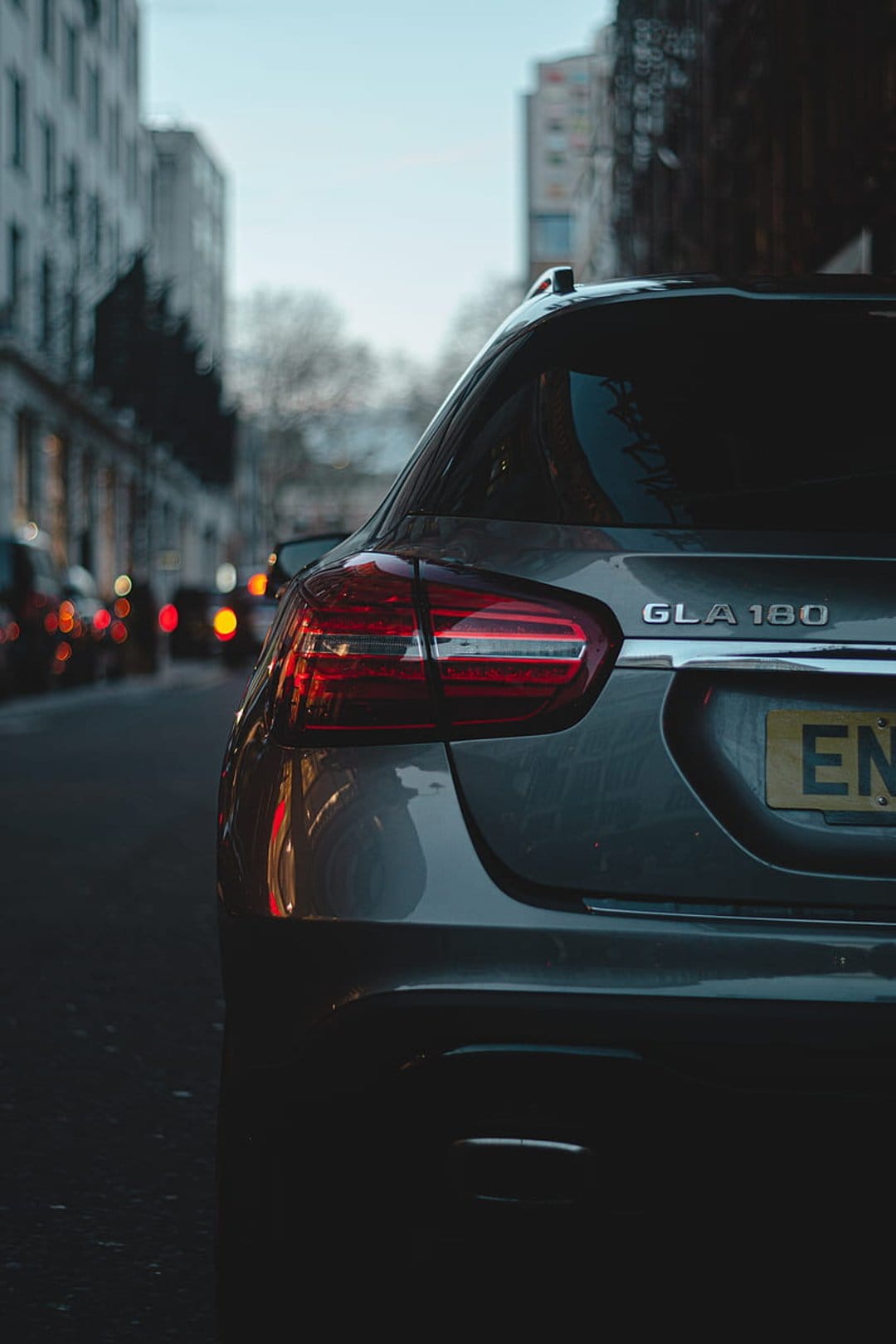 Mercedes GLA 180 rear with glowing red taillights parked on a moody city street with blurred night lights behind.