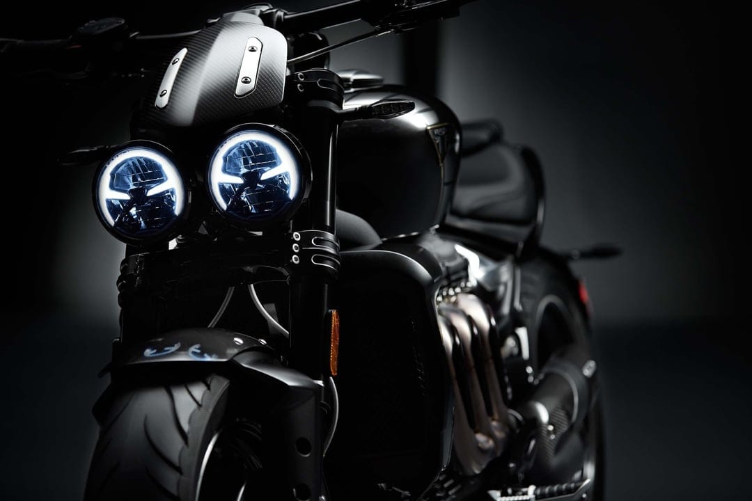 Twin glowing circular LED headlights on a black motorcycle with carbon fiber trim and dark studio lighting.