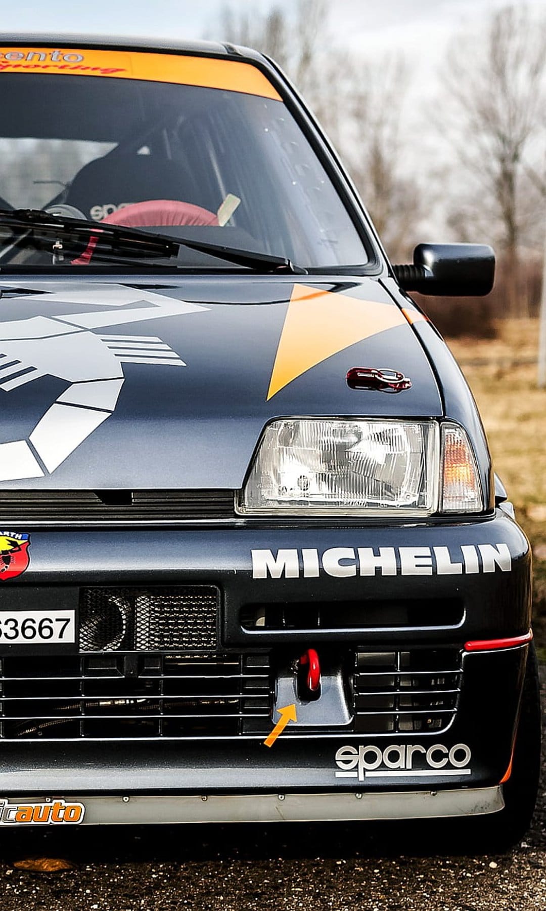 Abarth rally car front grille with a dark blue finish, Michelin branding, Sparco logo, and orange tow hook.