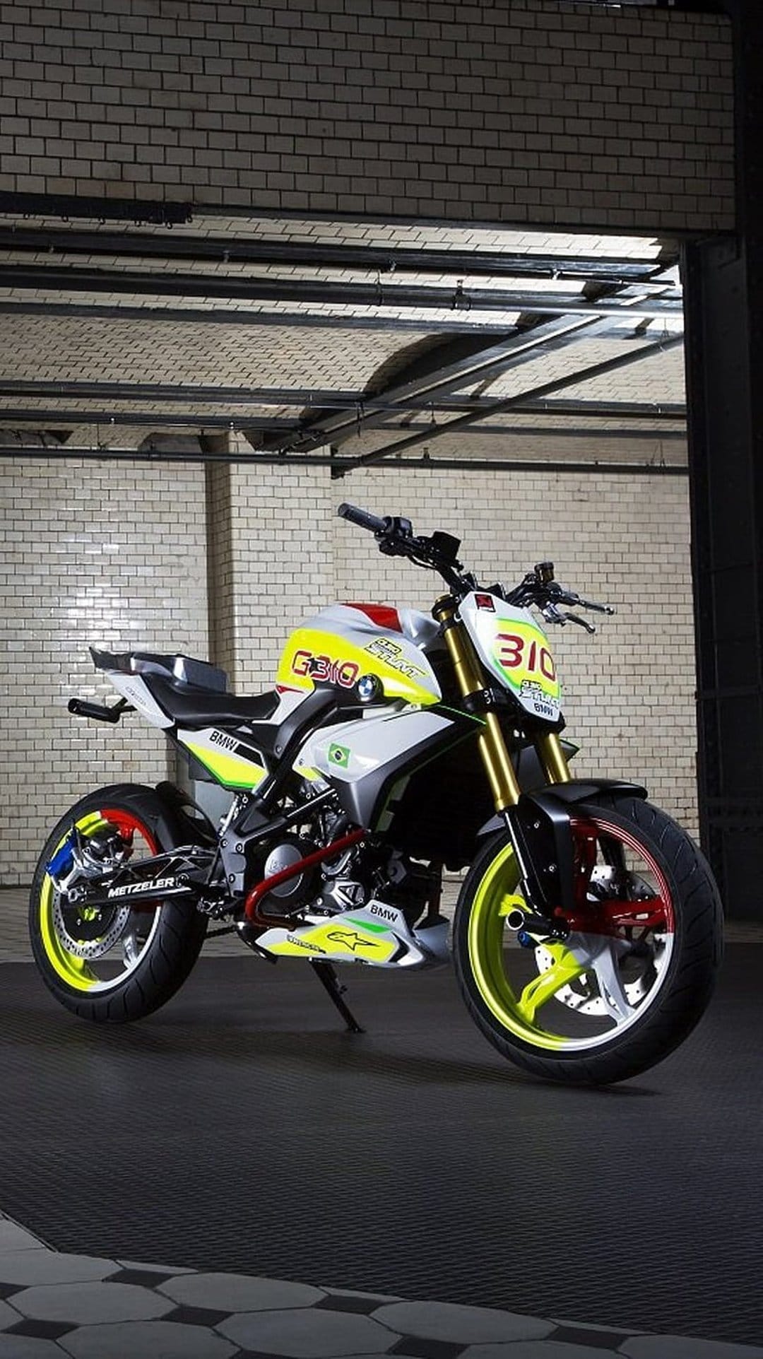 BMW G 310 R sport motorcycle with yellow and red decals parked against a textured industrial brick backdrop.
