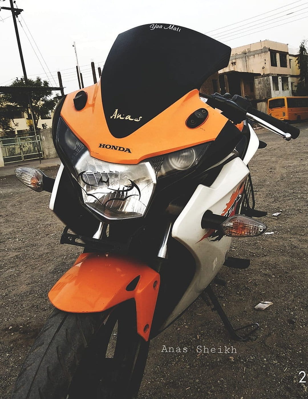 Honda motorcycle with orange fender and white bodywork shows its front tire and windshield in an urban setting.