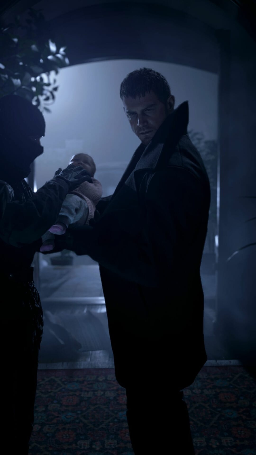 Chris Redfield in a dark coat holds a baby while standing in a dimly lit blue-toned doorway at night.
