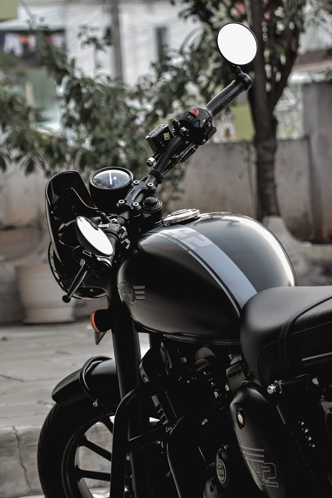 Black Jawa motorcycle with a grey stripe on the tank, chrome mirrors, and a round headlight against a blurred background.