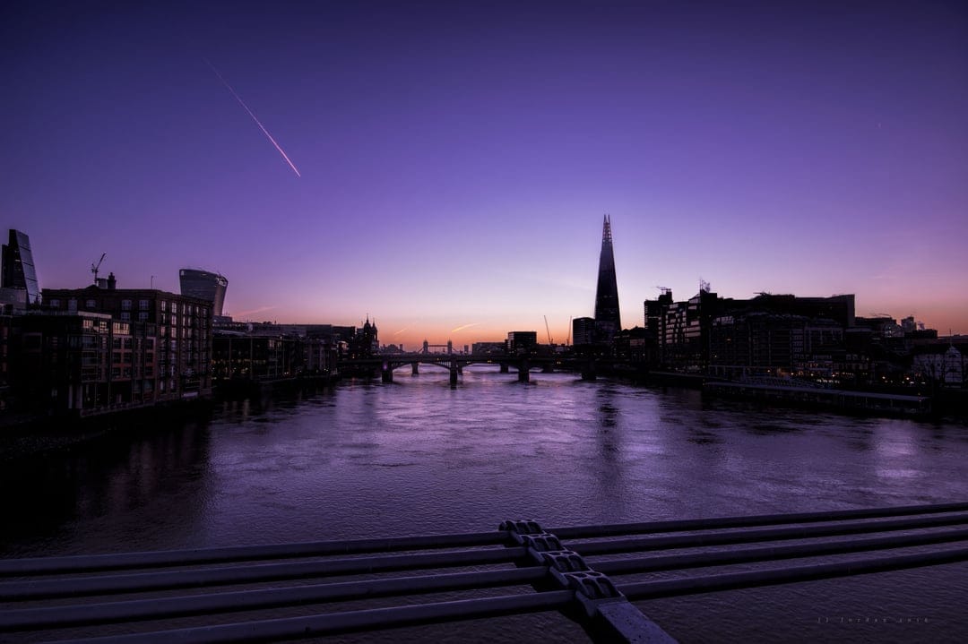 The Shard and London skyline silhouetted against a purple and orange sunset sky reflected in the River Thames.