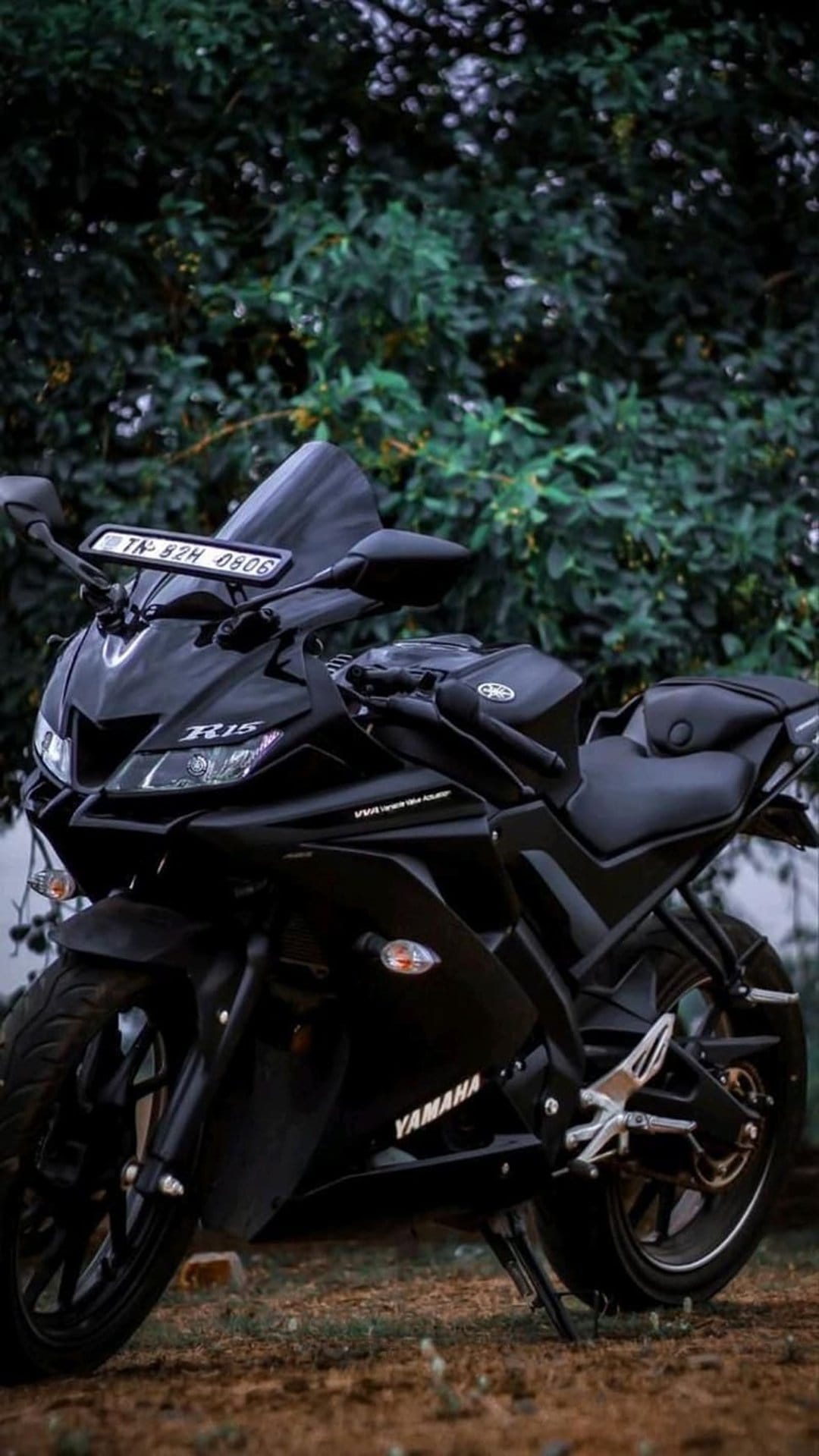 Black Yamaha R15 sportbike parked in a lush green forest with sharp matte fairings and natural lighting.