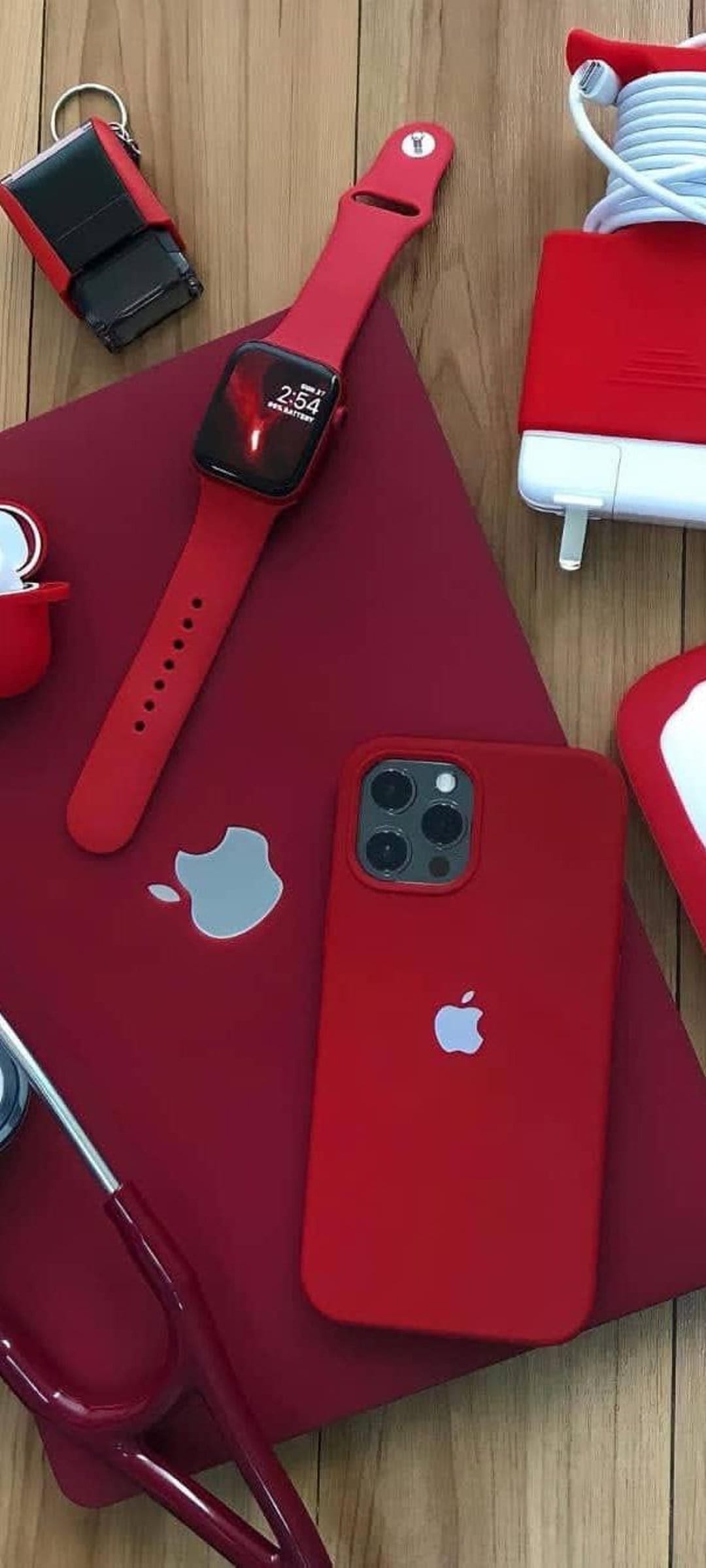 Red iPhone, Apple Watch, and AirPods arranged on wood beside a medical stethoscope and a matching crimson keychain.