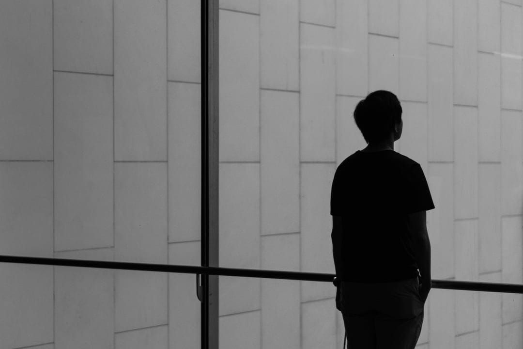 Person in silhouette faces a wall of rectangular tiles within a high-contrast black and white urban setting.