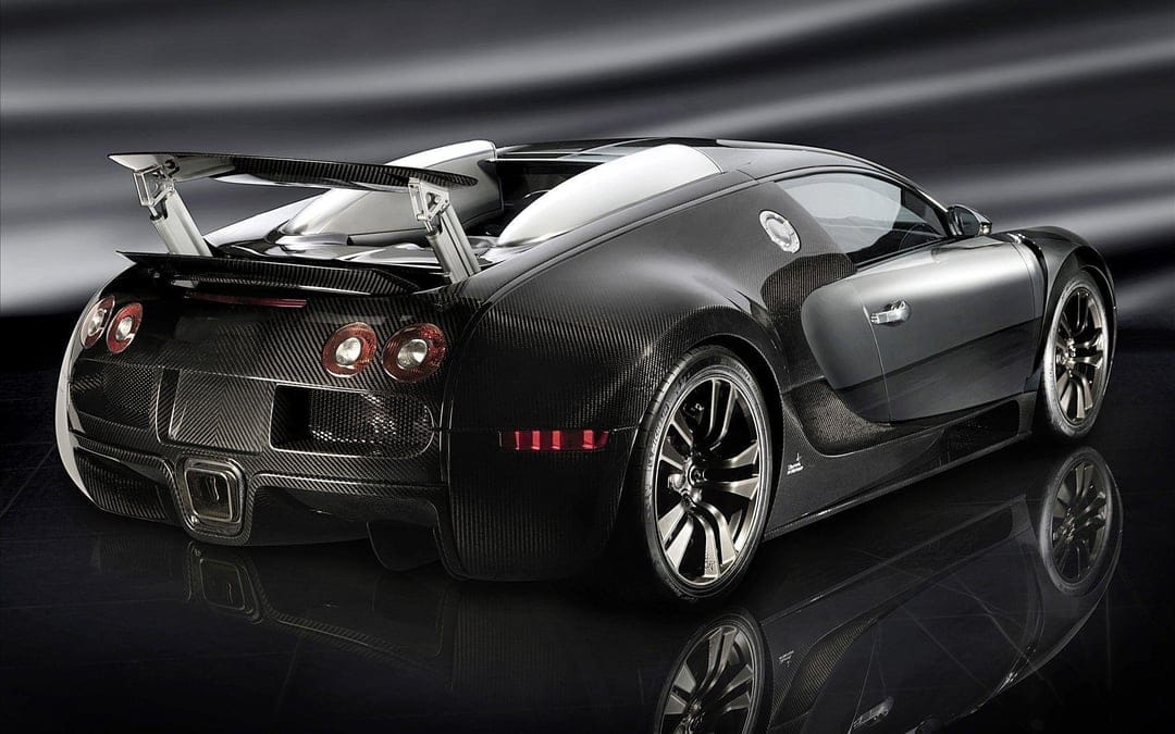 Rear view of a carbon fiber Bugatti Veyron supercar with an extended spoiler on a reflective dark surface.