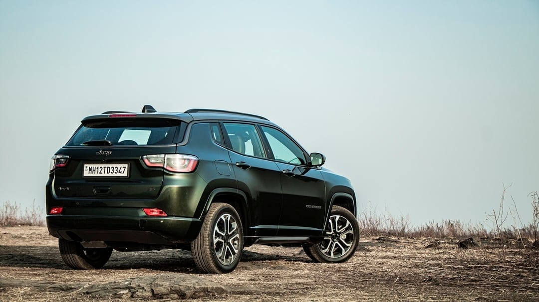 Dark green Jeep Compass 4x4 SUV parked on a dry grassy field under a clear sky at a low camera angle.