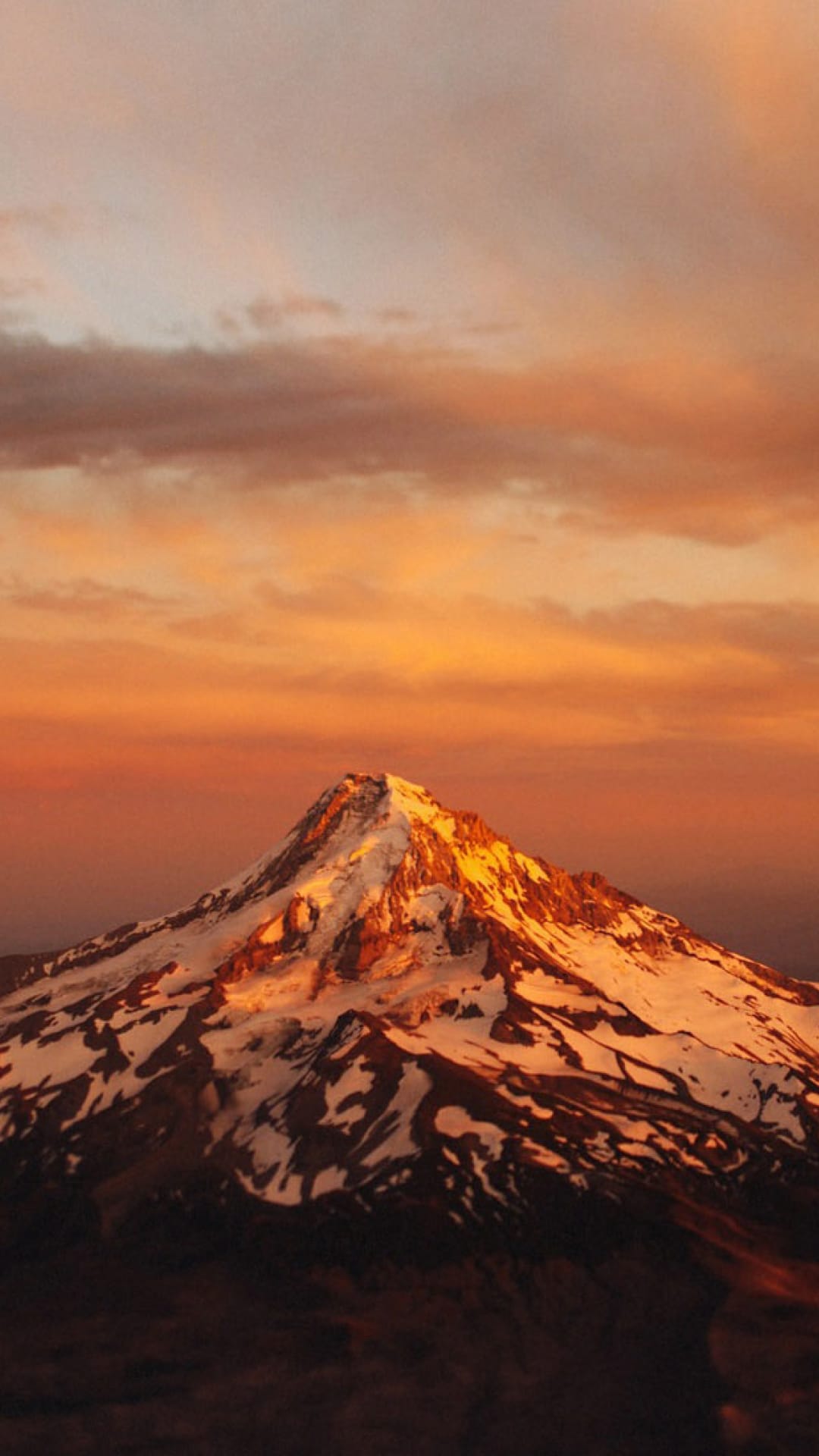 Mount Hood peak covered in white snow reflecting orange sunset light against a soft pink and grey twilight sky.