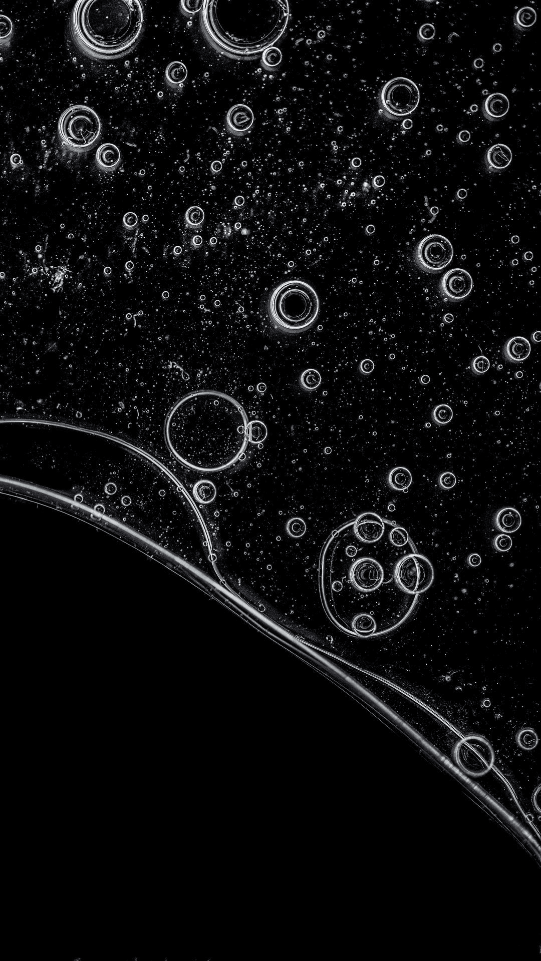Spherical translucent bubbles with sharp highlights drift through a deep black liquid in a macro close-up view.