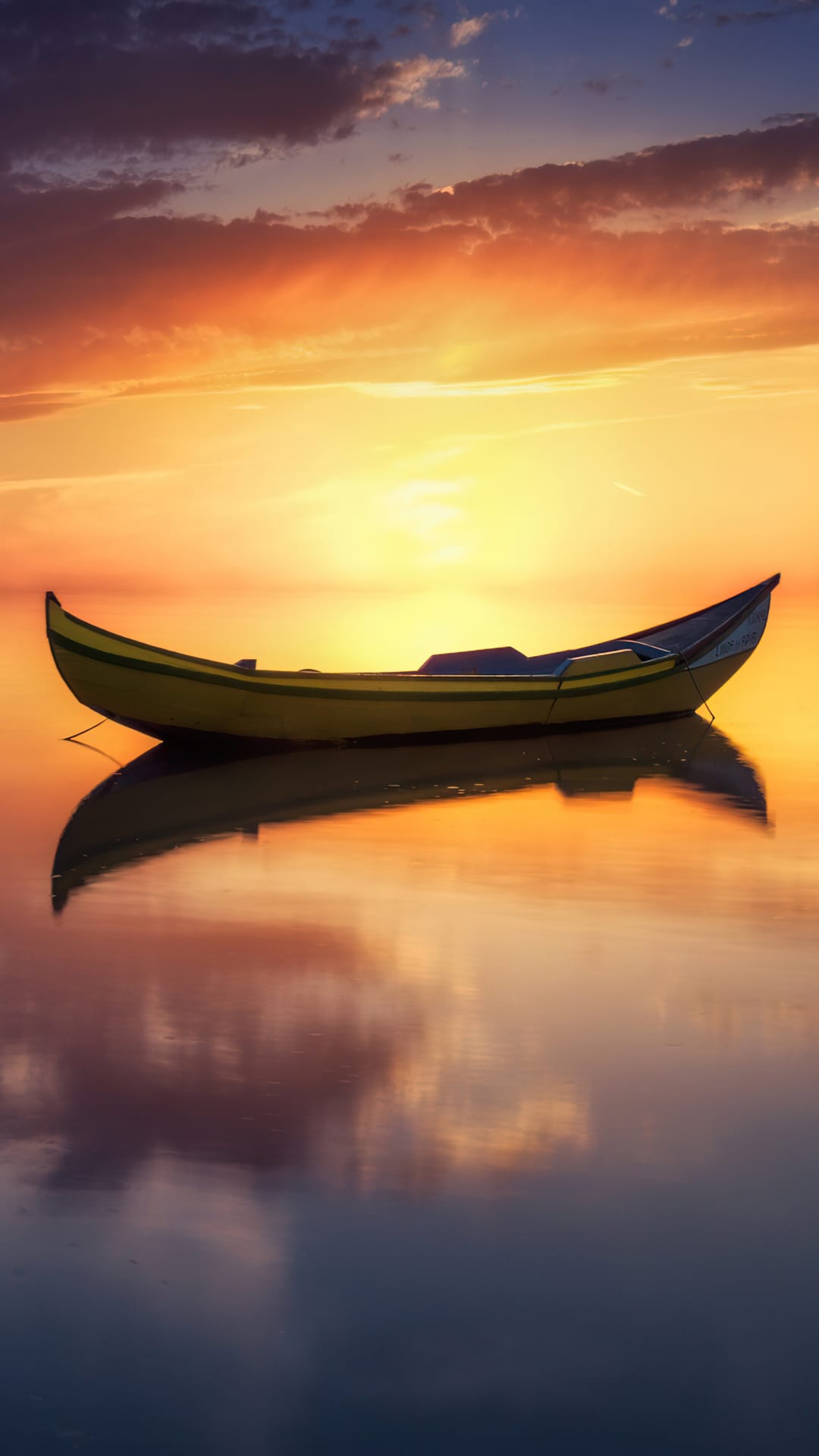 Yellow boat rests on calm water reflecting a vibrant orange and purple sunset sky on a clear evening horizon.