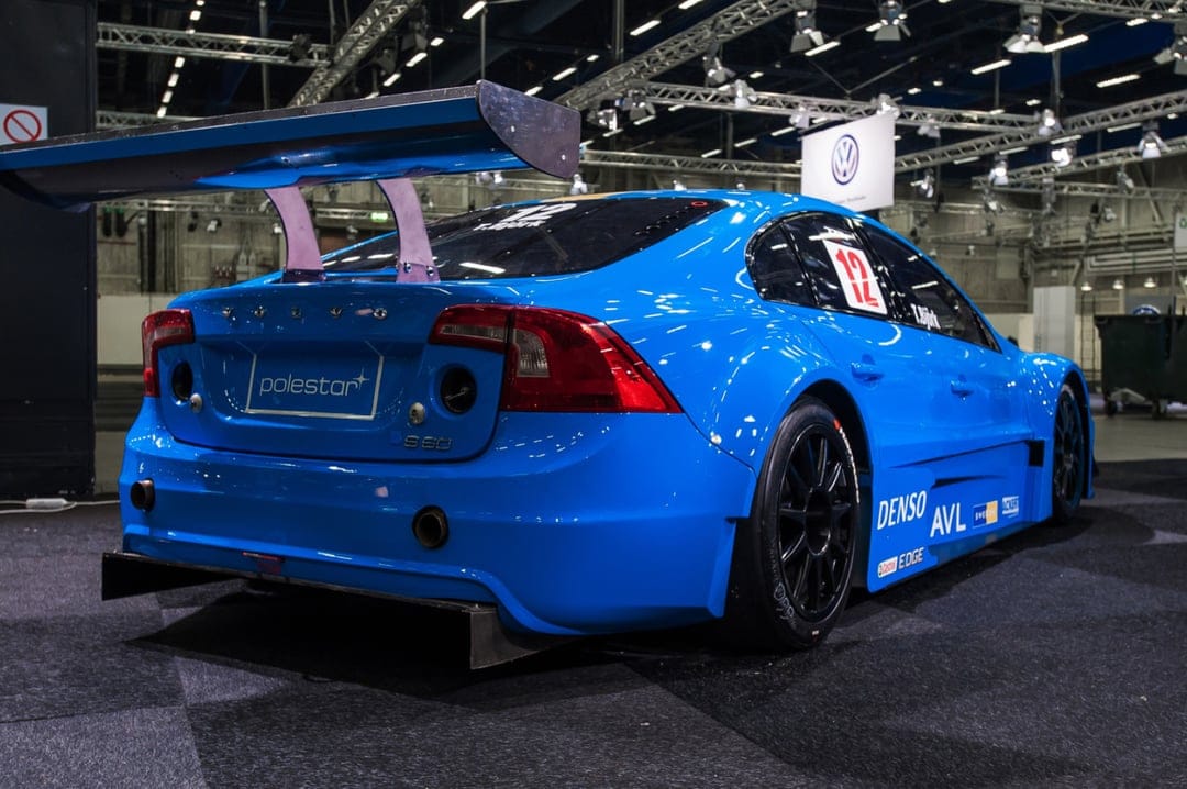 Rear view of a blue Volvo S60 Polestar racing car with a large spoiler and wide body kit in an indoor hall.
