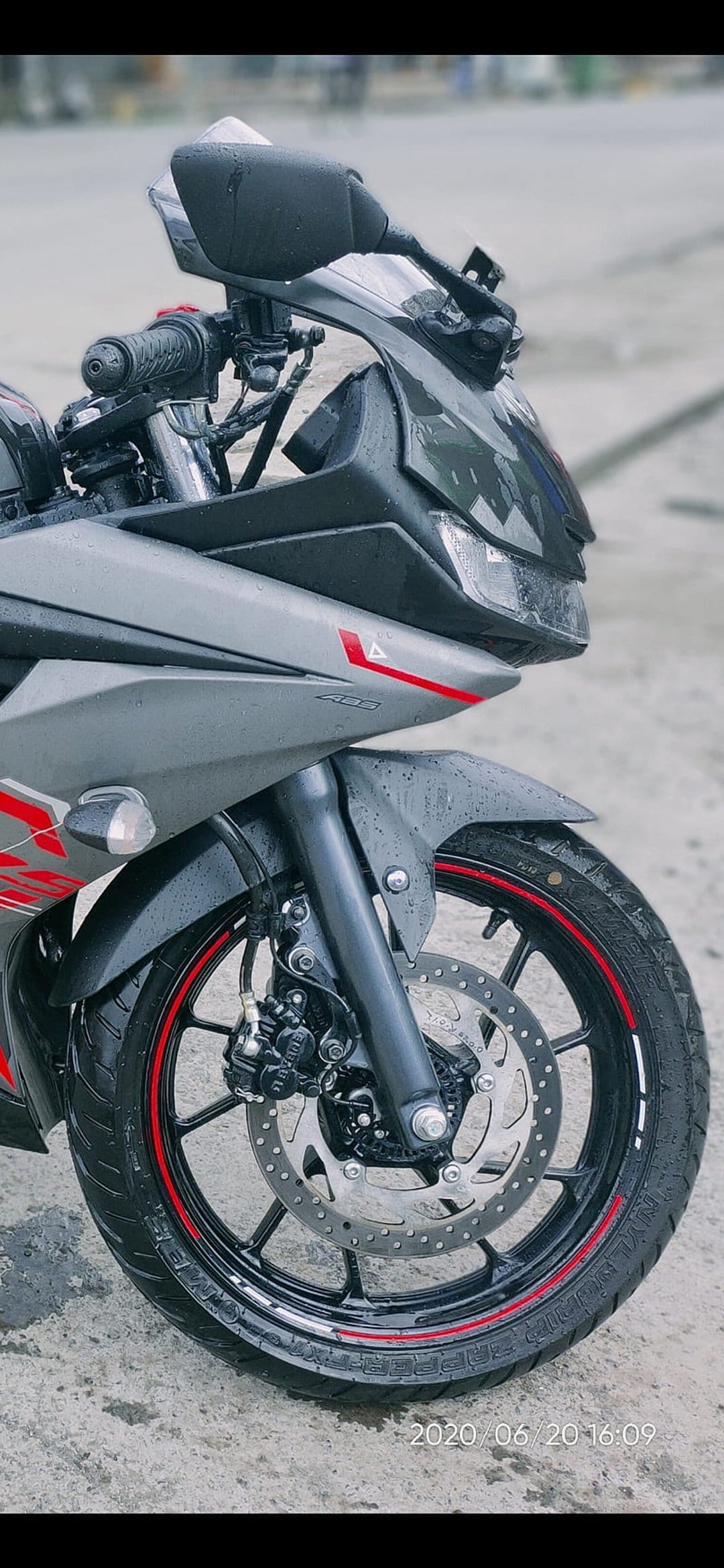 Yamaha R15 front wheel assembly covered in raindrops with a grey fairing, red rim tape, and a metal brake disc.