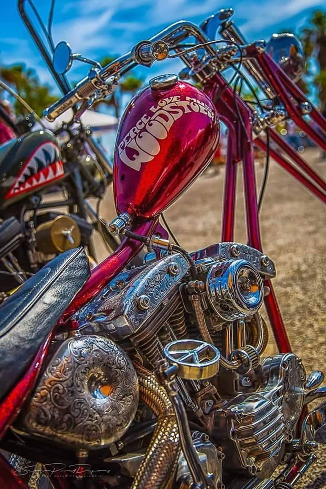 Red chopper motorcycle with a Woodstock fuel tank graphic, chrome engine parts, and a shark-mouth front fender.