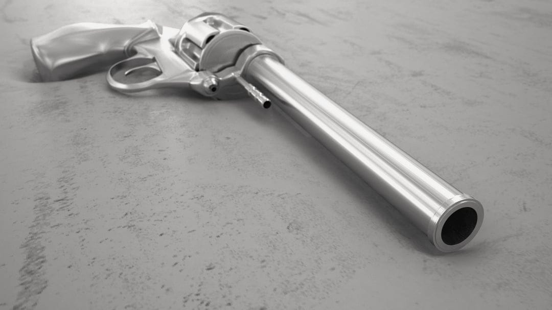 Chrome revolver with a long barrel and polished cylinder lies on a gritty grey stone textured surface.