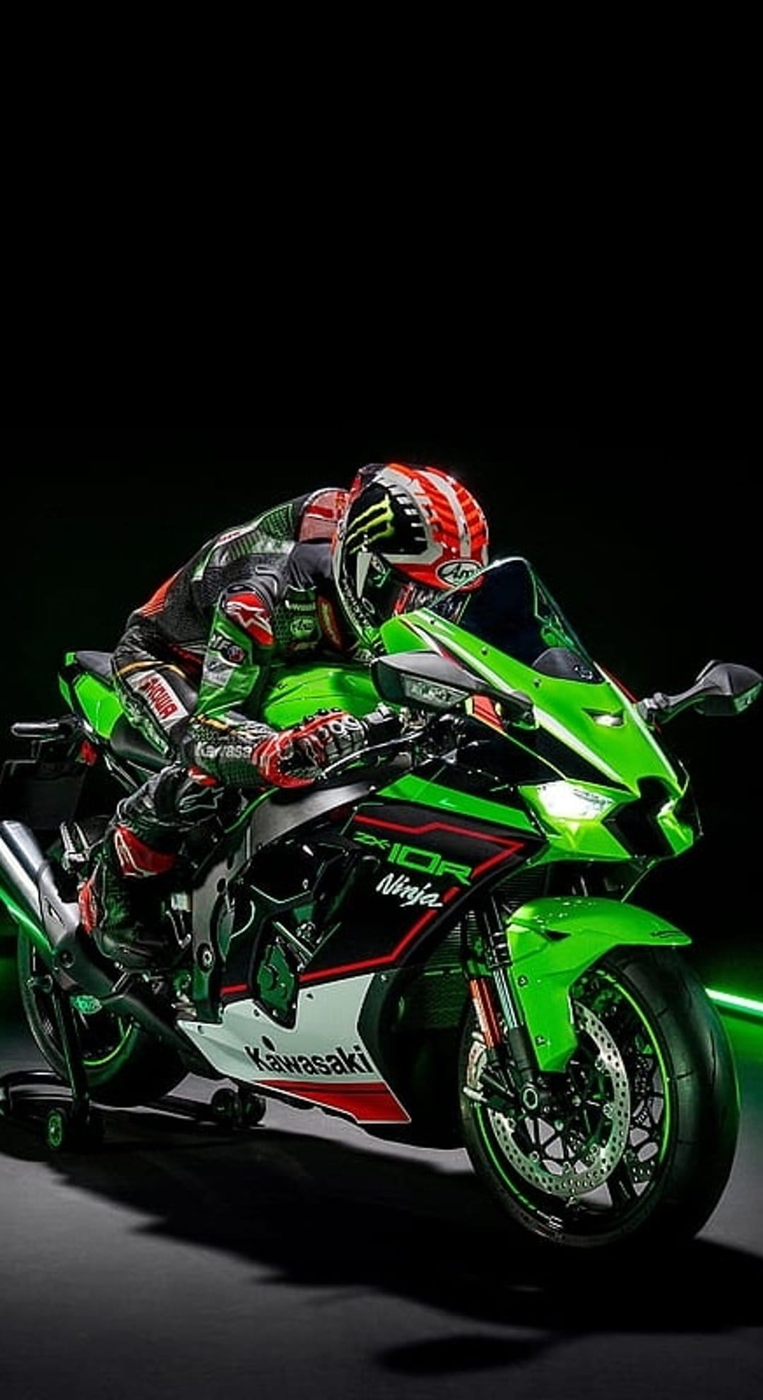 Professional racer on a lime green Kawasaki Ninja ZX-10R motorcycle leaning into a corner in dark studio lighting.