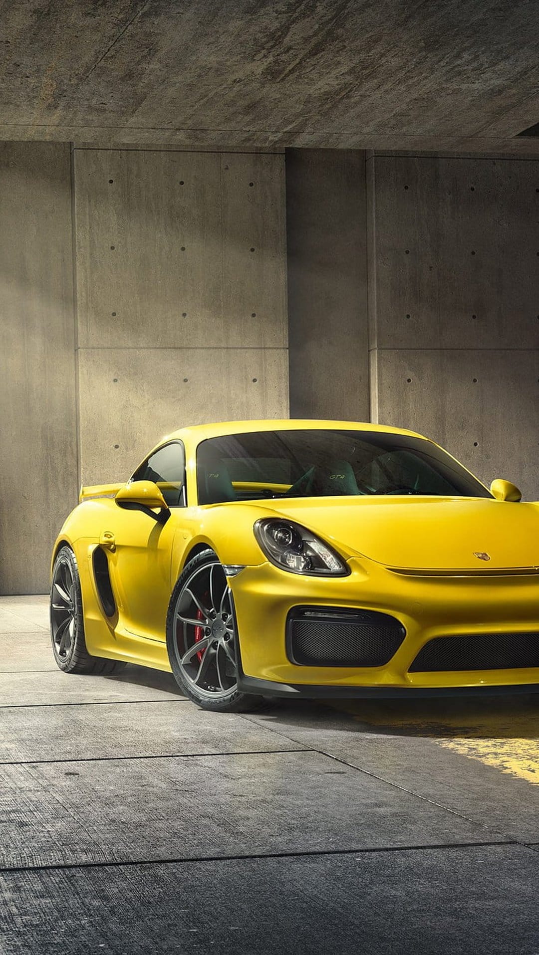 Porsche Cayman GT4 in yellow parked on a textured concrete floor inside a minimalist industrial garage.
