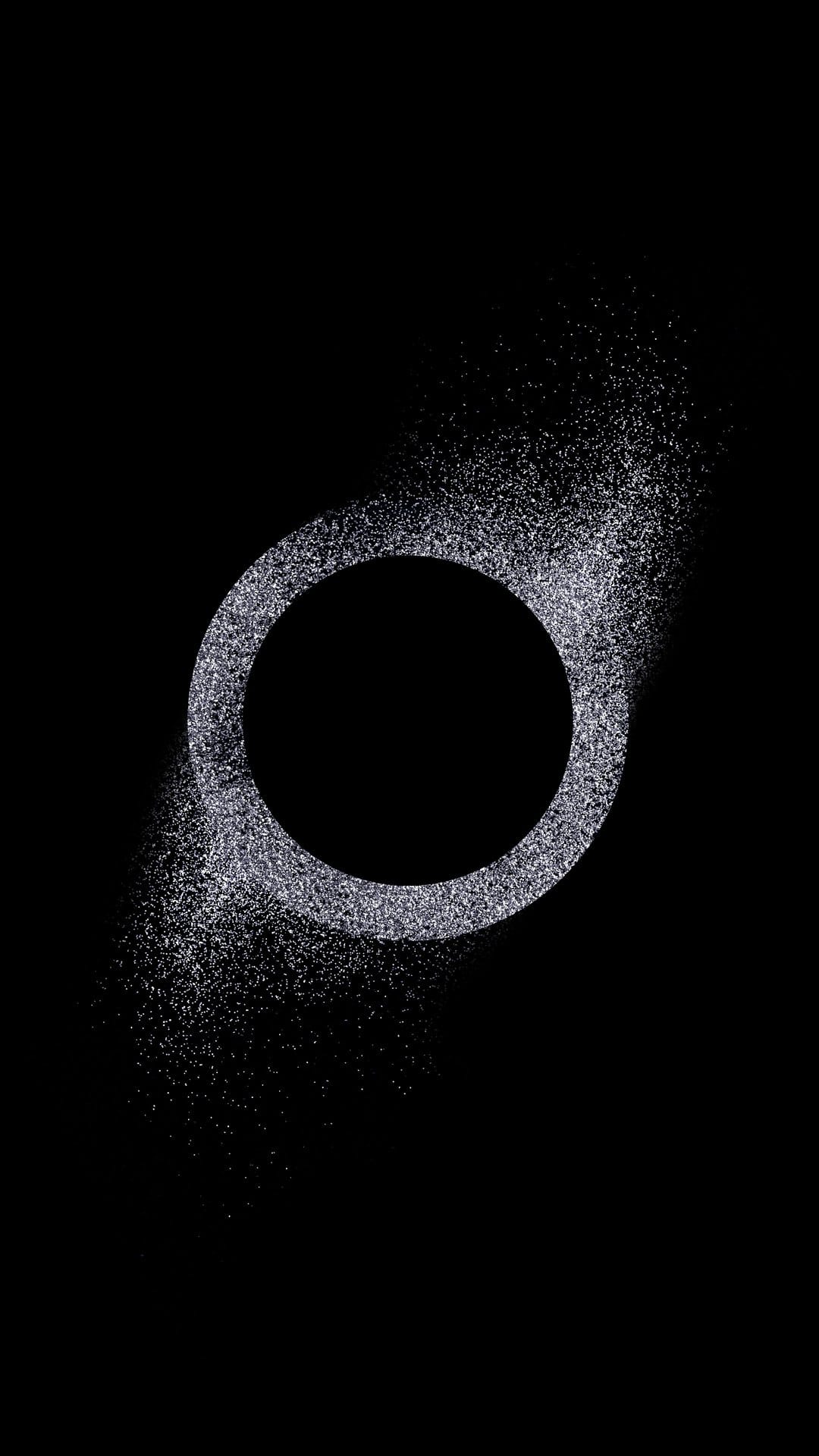 Silver glitter ring with trailing particles glows against a solid black background in a vertical format.