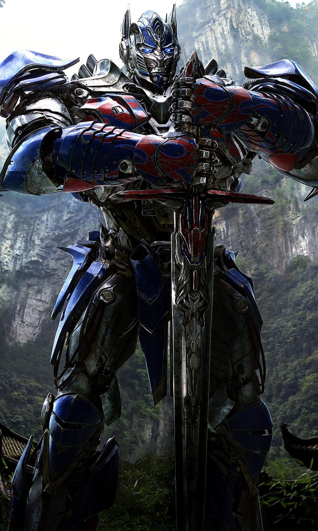 Optimus Prime stands in a forest holding a large sword while wearing detailed red and blue robotic armor.