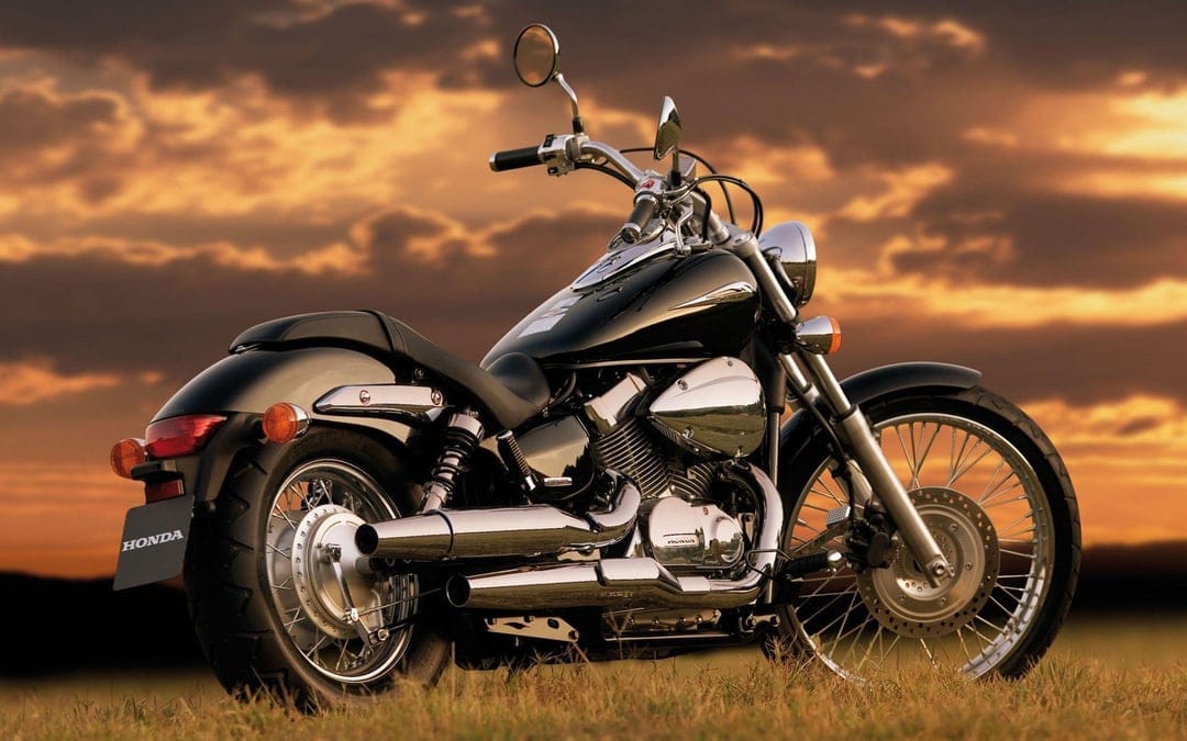 Black Honda cruiser motorcycle parked in a field under a dramatic orange and gold sunset sky with chrome accents.
