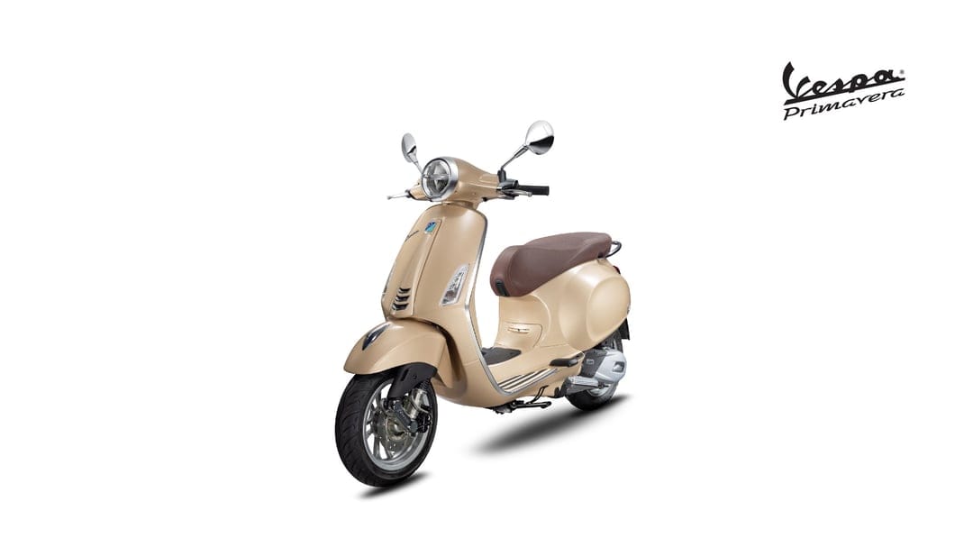 Beige Vespa Primavera scooter with a brown seat and chrome mirrors on a minimalist white background.