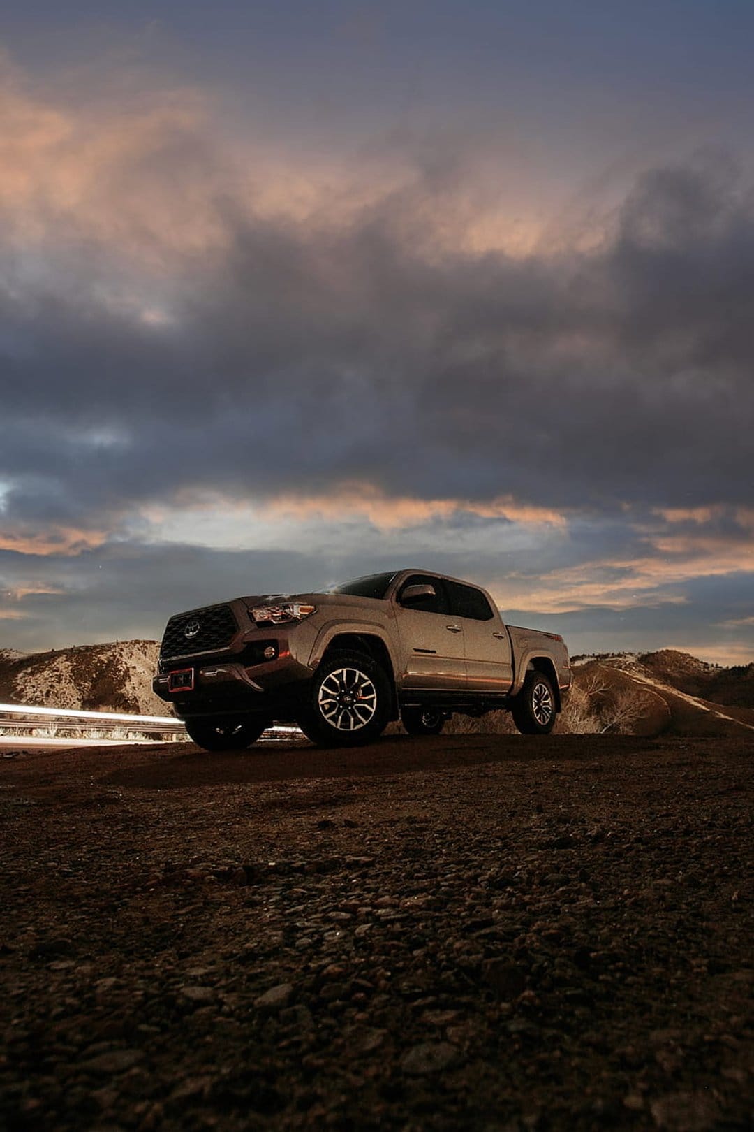 Silver Toyota Tacoma parked on rocky terrain with light streaks and a purple sunset sky in the background.