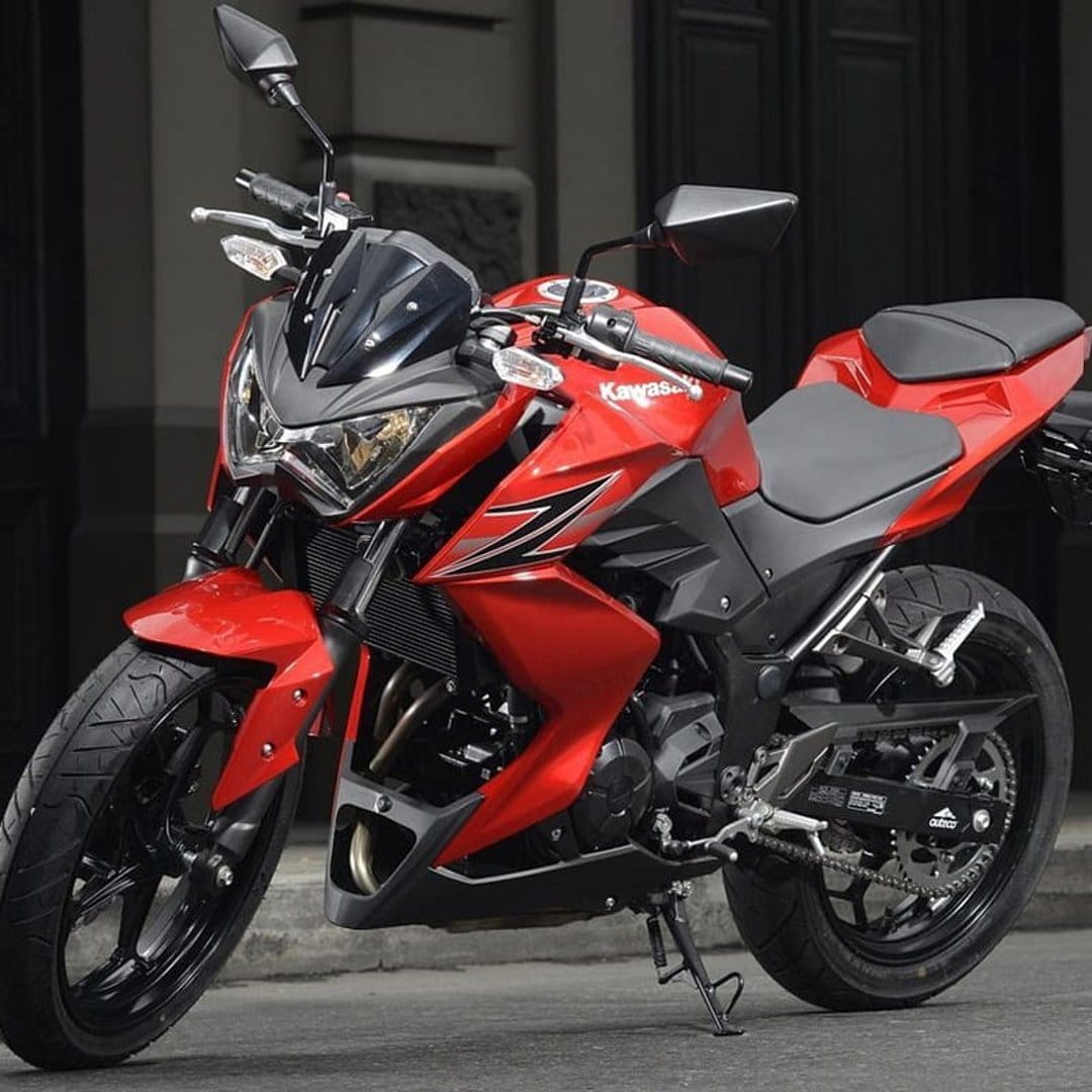 Red Kawasaki Z250 motorcycle featuring sharp fairings and black accents parked on pavement with urban bokeh.