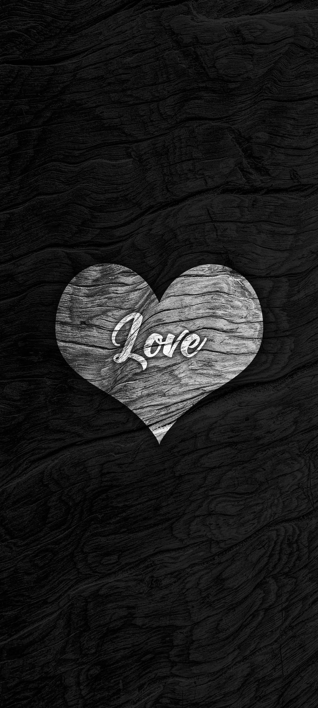 Weathered wooden heart with the word Love carved in script over a dark, textured timber plank background.
