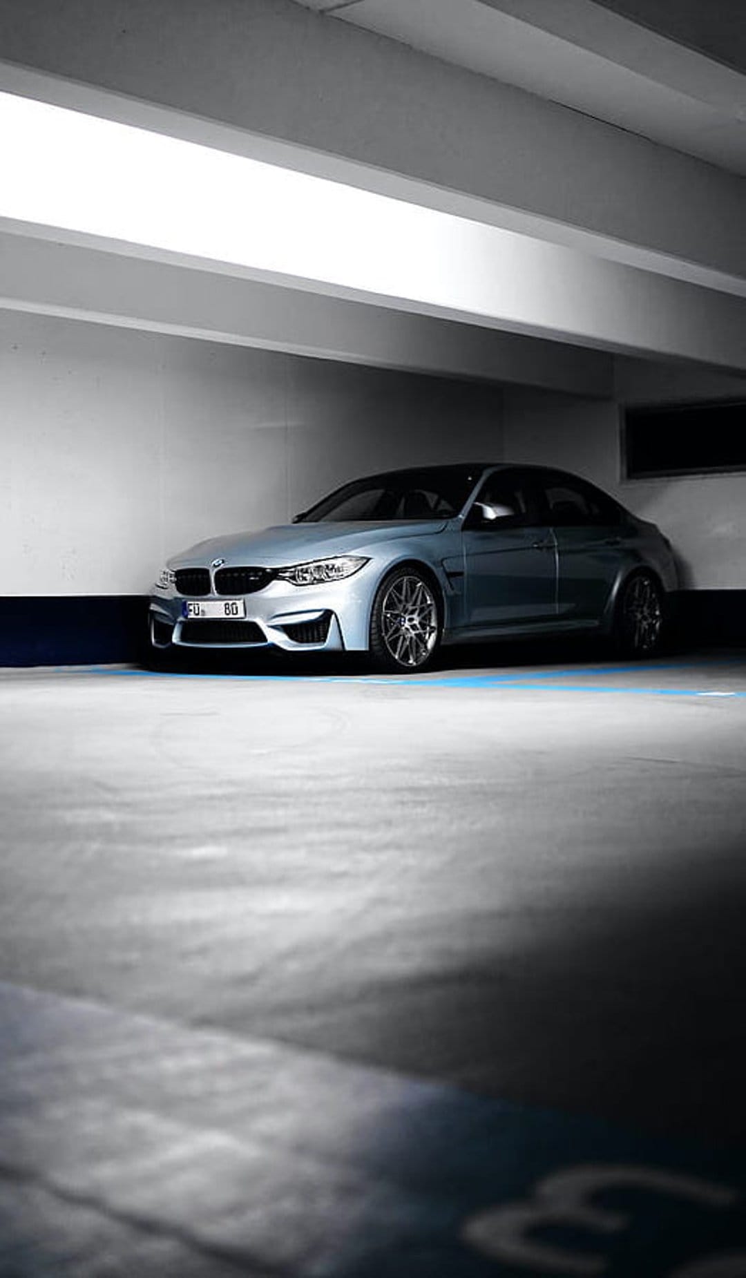 Silver BMW M4 coupe parked on a concrete garage floor under dim ambient lighting with visible alloy wheels.