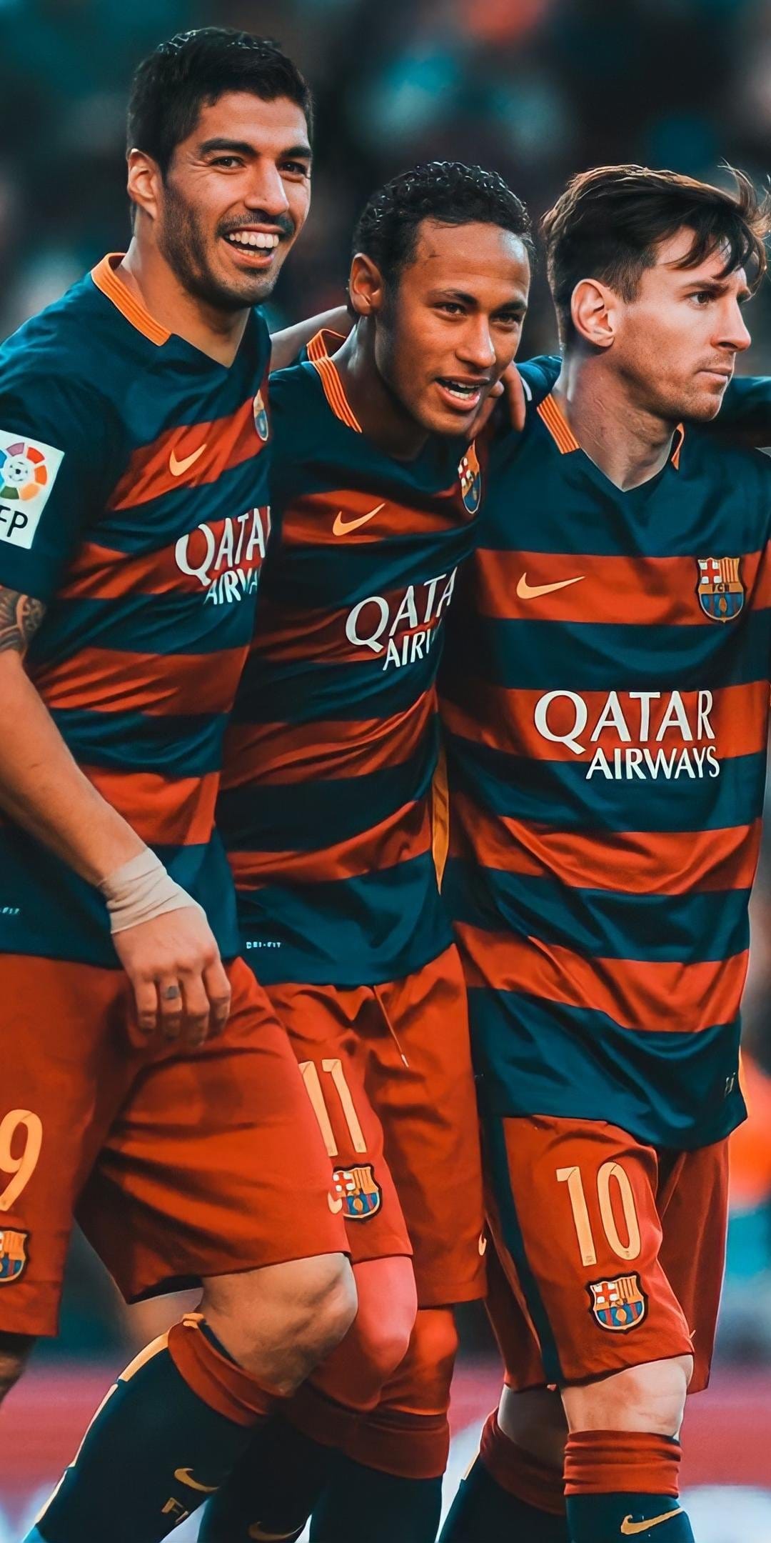 Lionel Messi, Luis Suarez, and Neymar Jr. cheer together on a grass pitch wearing striped Barcelona jerseys.