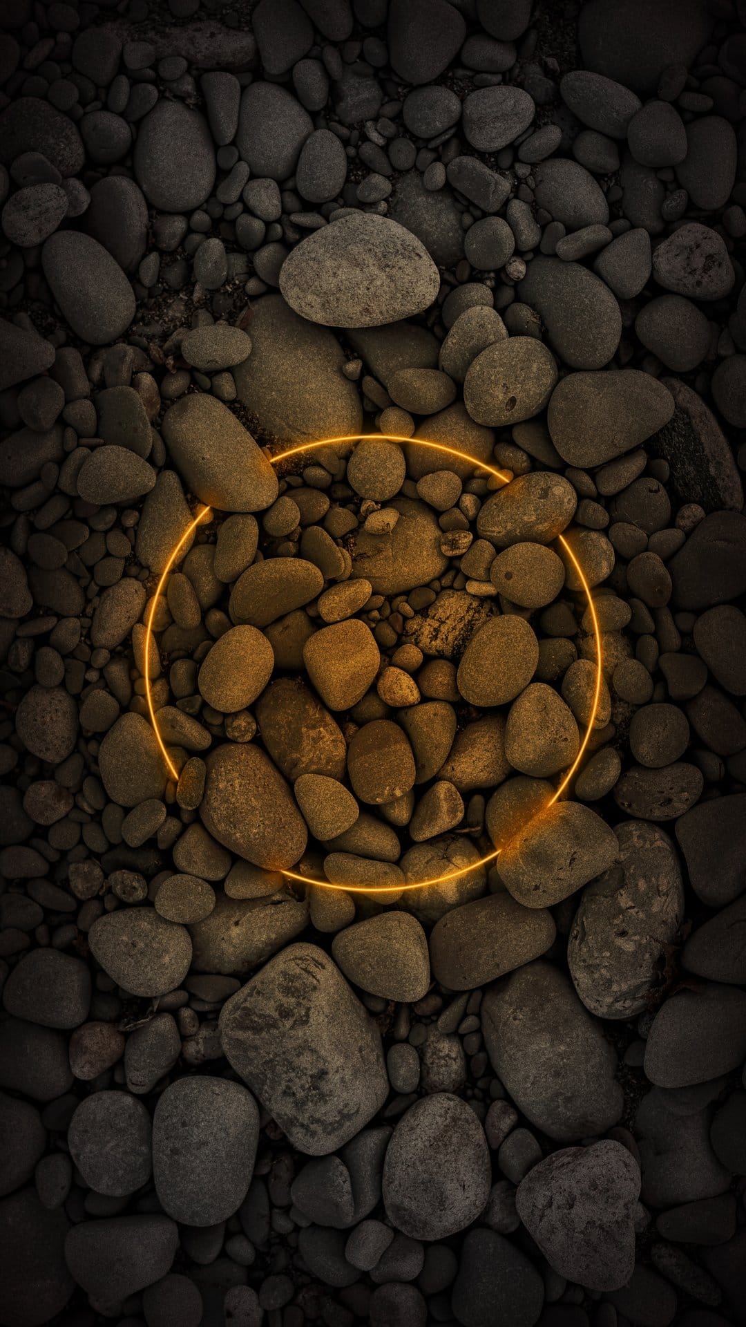 Glowing orange neon ring centered over a dense collection of smooth dark grey river pebbles in a top-down view.