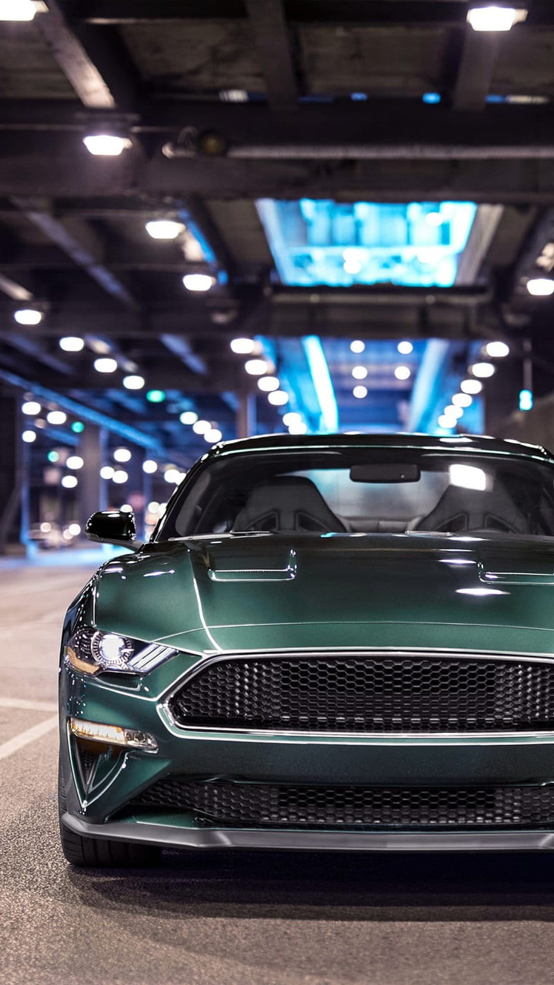 Dark green Ford Mustang front view parked inside an illuminated urban tunnel with glowing yellow overhead lights.