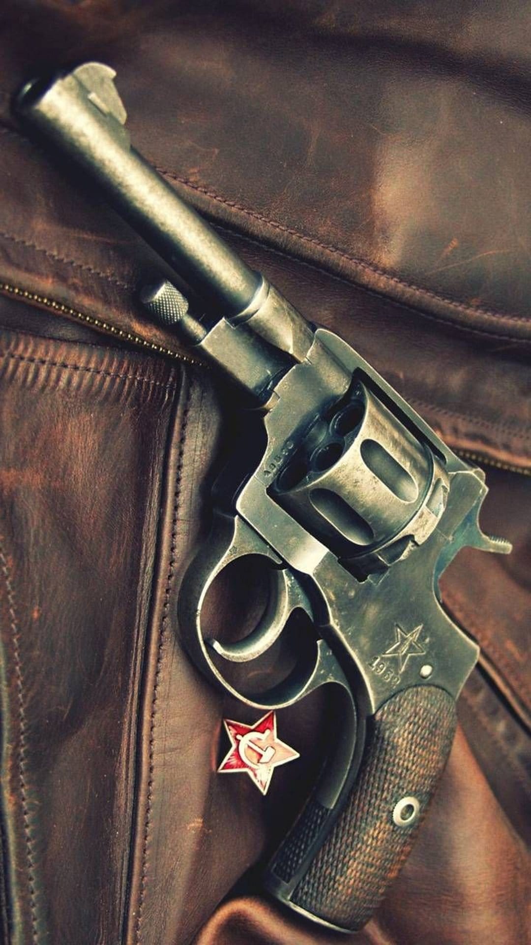 Vintage Nagant revolver with a red star emblem resting on textured brown leather with visible metallic wear.