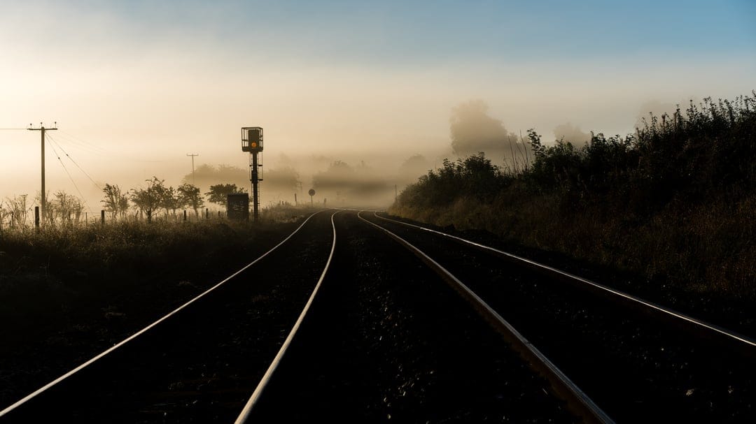 Train tracks receding into a dense golden mist at dawn with a signal box silhouette in the background.