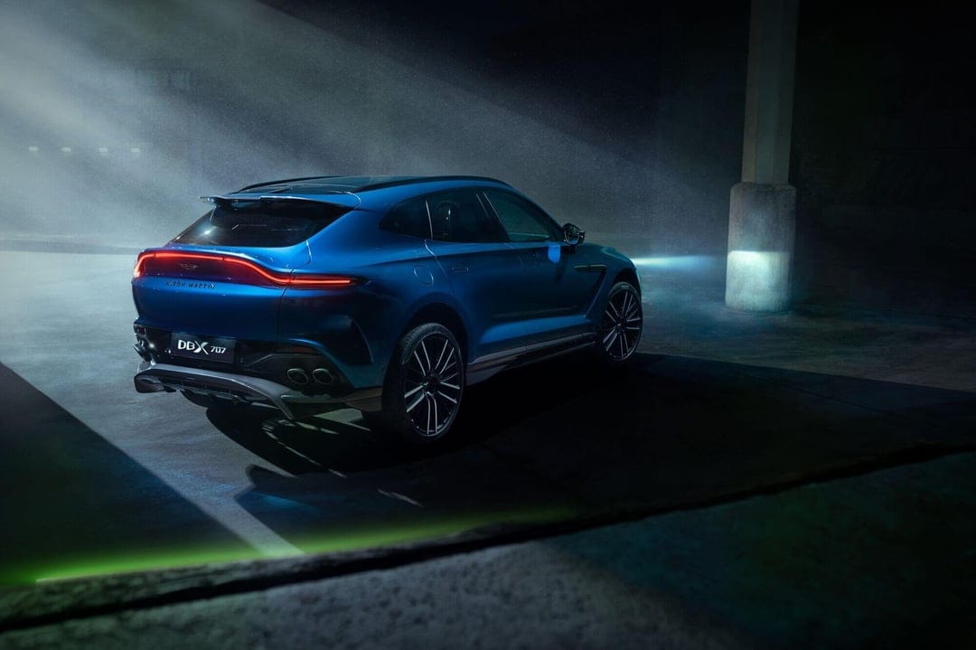 Blue Aston Martin DBX 707 luxury SUV with glowing red taillights in a dark foggy industrial garage.