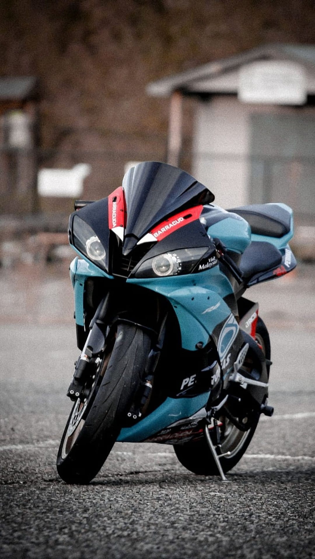 Aqua and black sportbike motorcycle parked on textured asphalt from a low angle against a blurred urban backdrop.