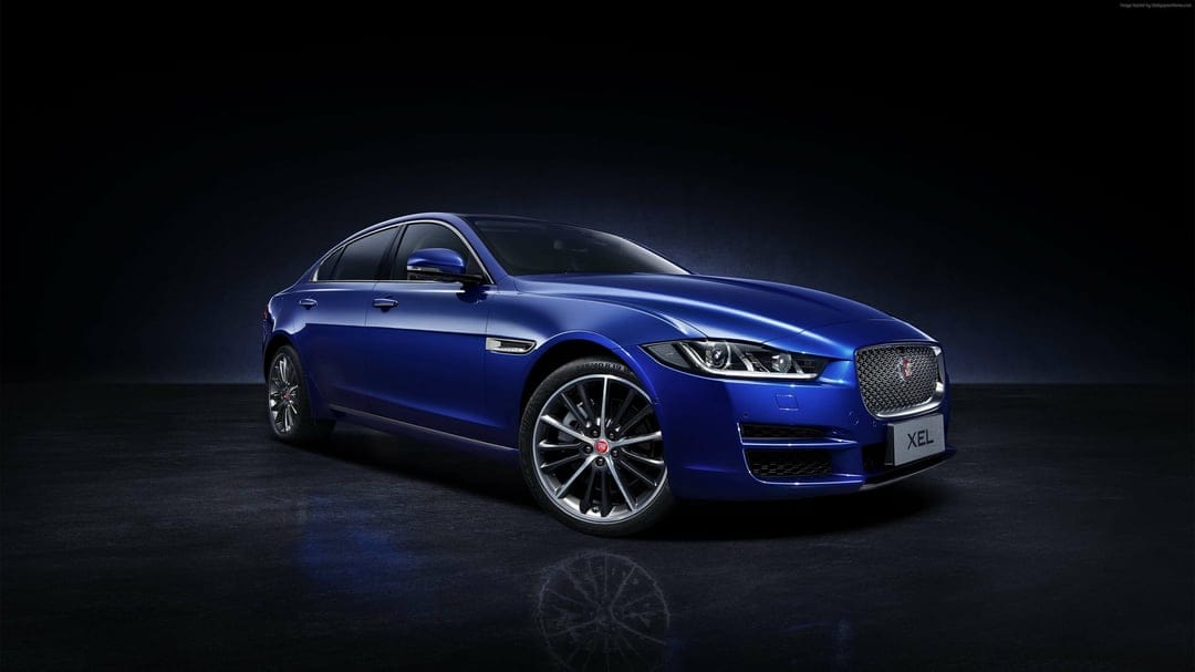 Blue Jaguar XEL luxury sedan parked in a dark studio with dramatic lighting and a subtle floor reflection.