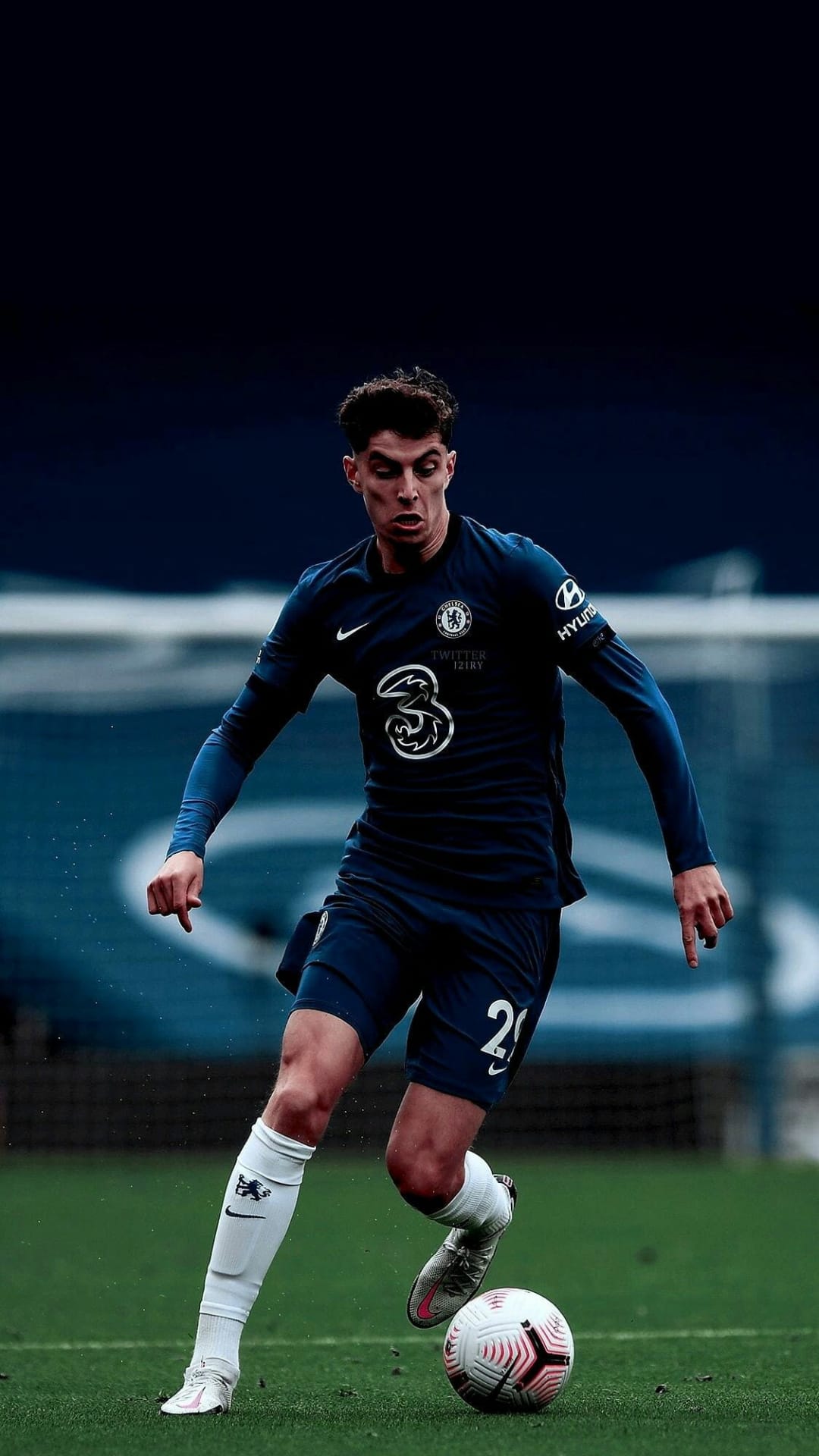 Kai Havertz in a blue Chelsea jersey runs with a football on a green grass field during a professional match.