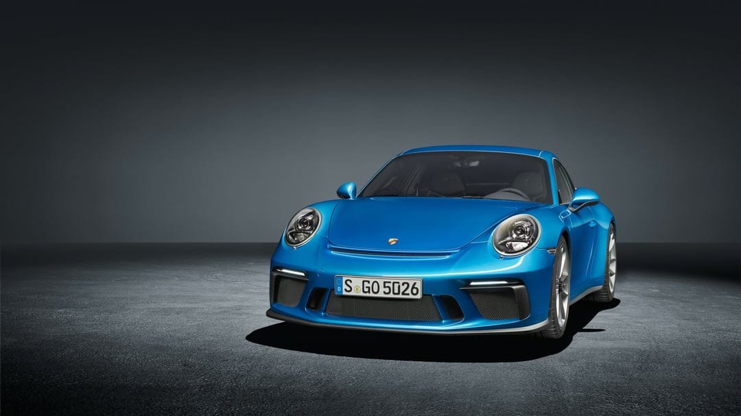 Blue Porsche 911 GT3 sports car parked on a textured dark floor in a minimalist gray studio setting.