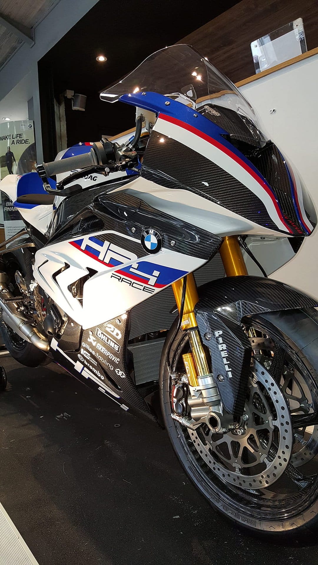 BMW HP4 Race motorcycle with carbon fiber bodywork, gold Öhlins forks, and Brembo brakes on a dark background.