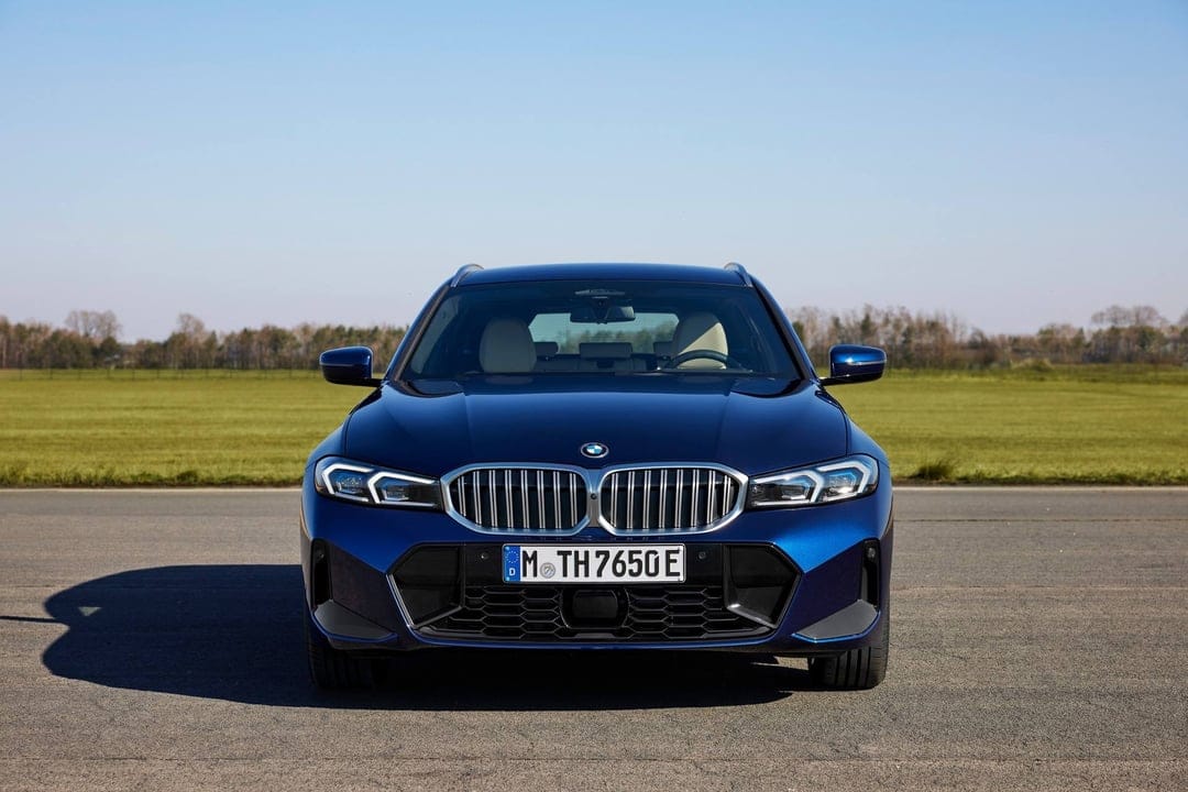 Dark blue BMW parked on an asphalt track with a green field and a clear blue sky in the background.
