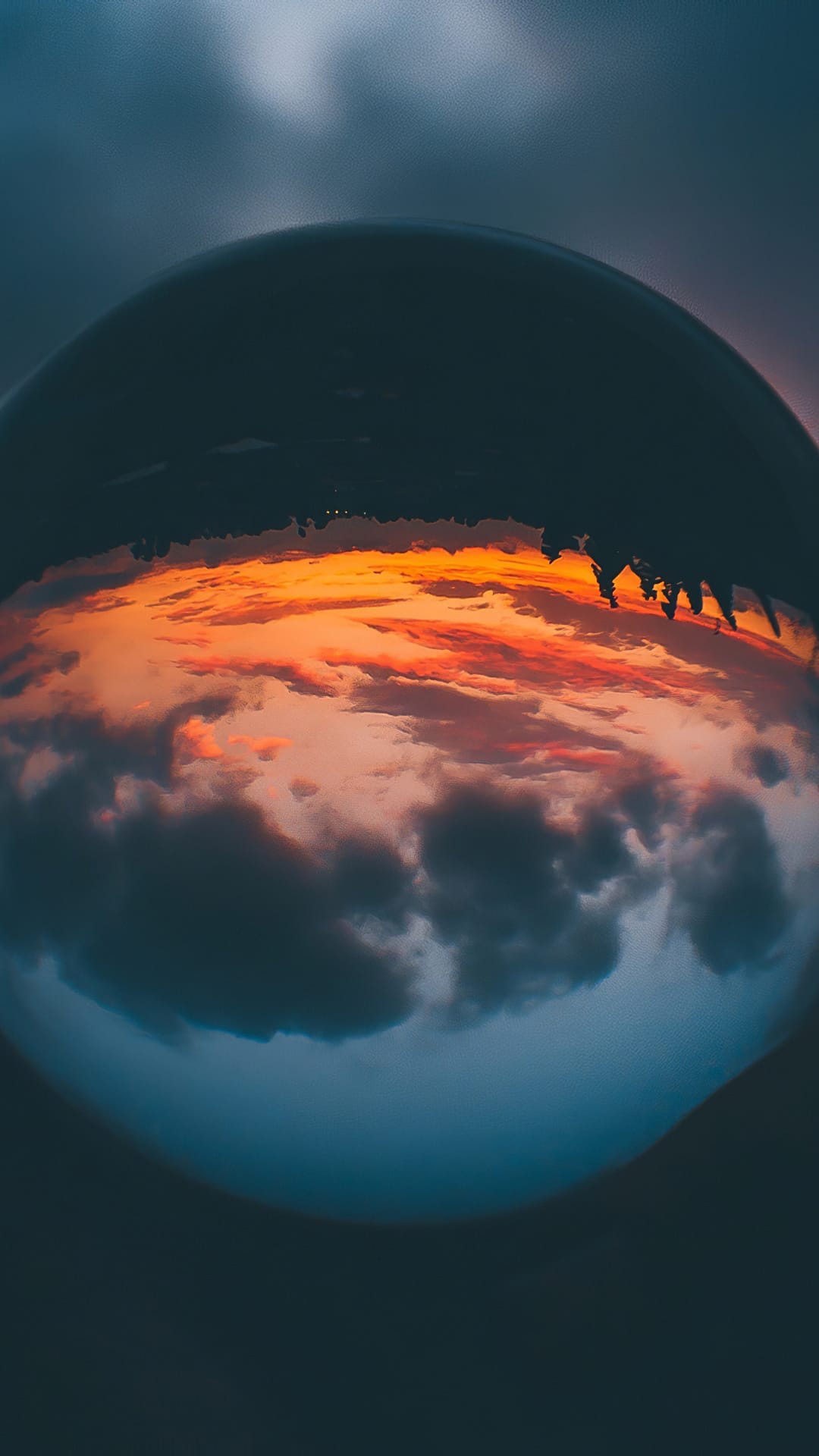 Clear glass sphere containing an inverted reflection of orange sunset clouds against a blurred horizon backdrop.