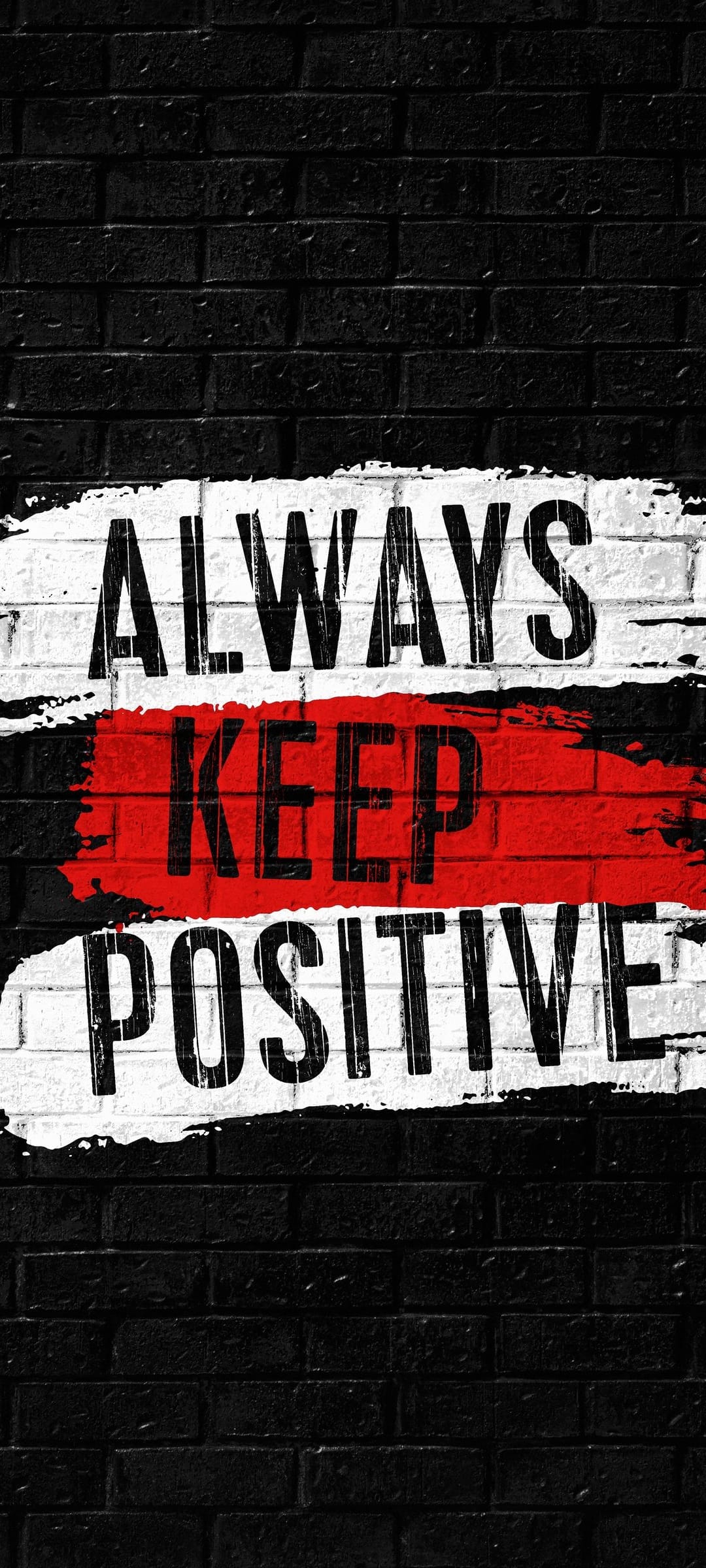 Always Keep Positive text with a red stripe accents a textured black brick masonry wall in close-up detail.