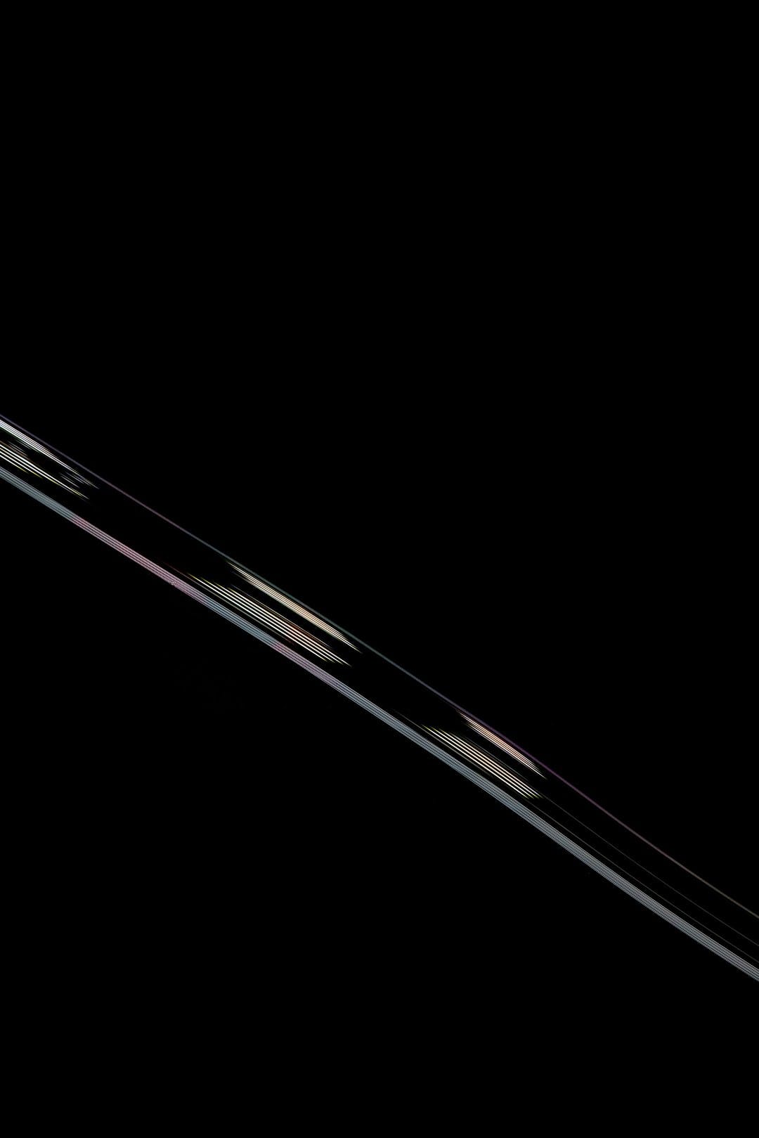 Diagonal rainbow light beam with iridescent edges cutting across a solid matte black vertical background.