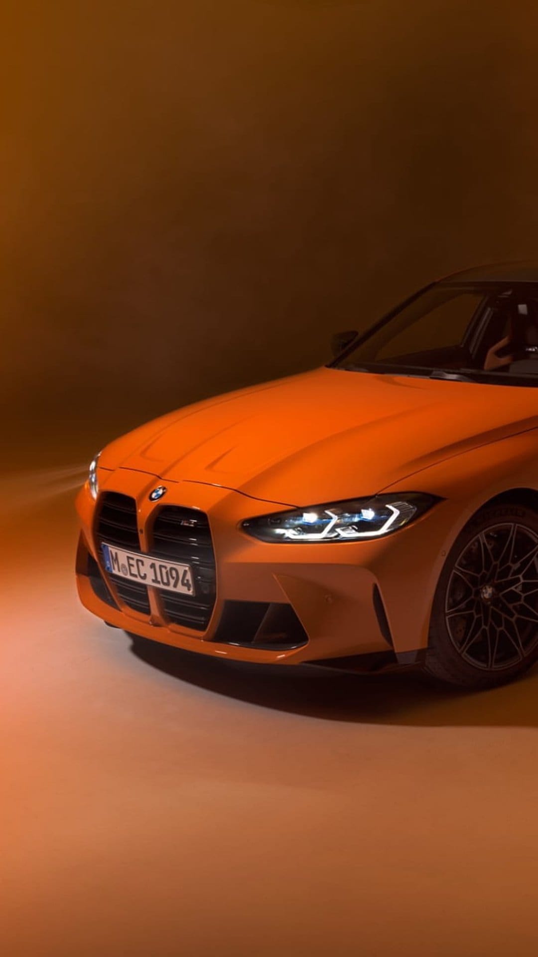 Orange BMW M4 Coupe front end with black kidney grille, sharp LED headlights, and dark alloy wheels on display.