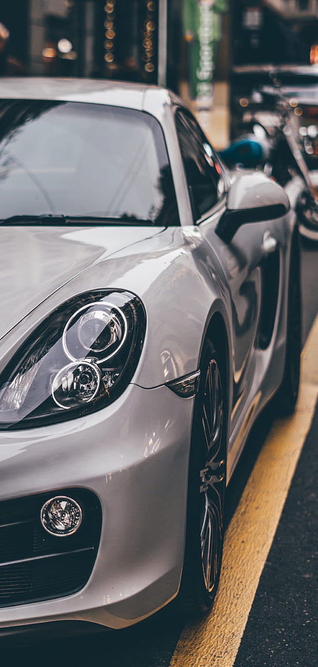 Silver Porsche Cayman with round headlights and metallic body parked on a dark city street with yellow road lines.