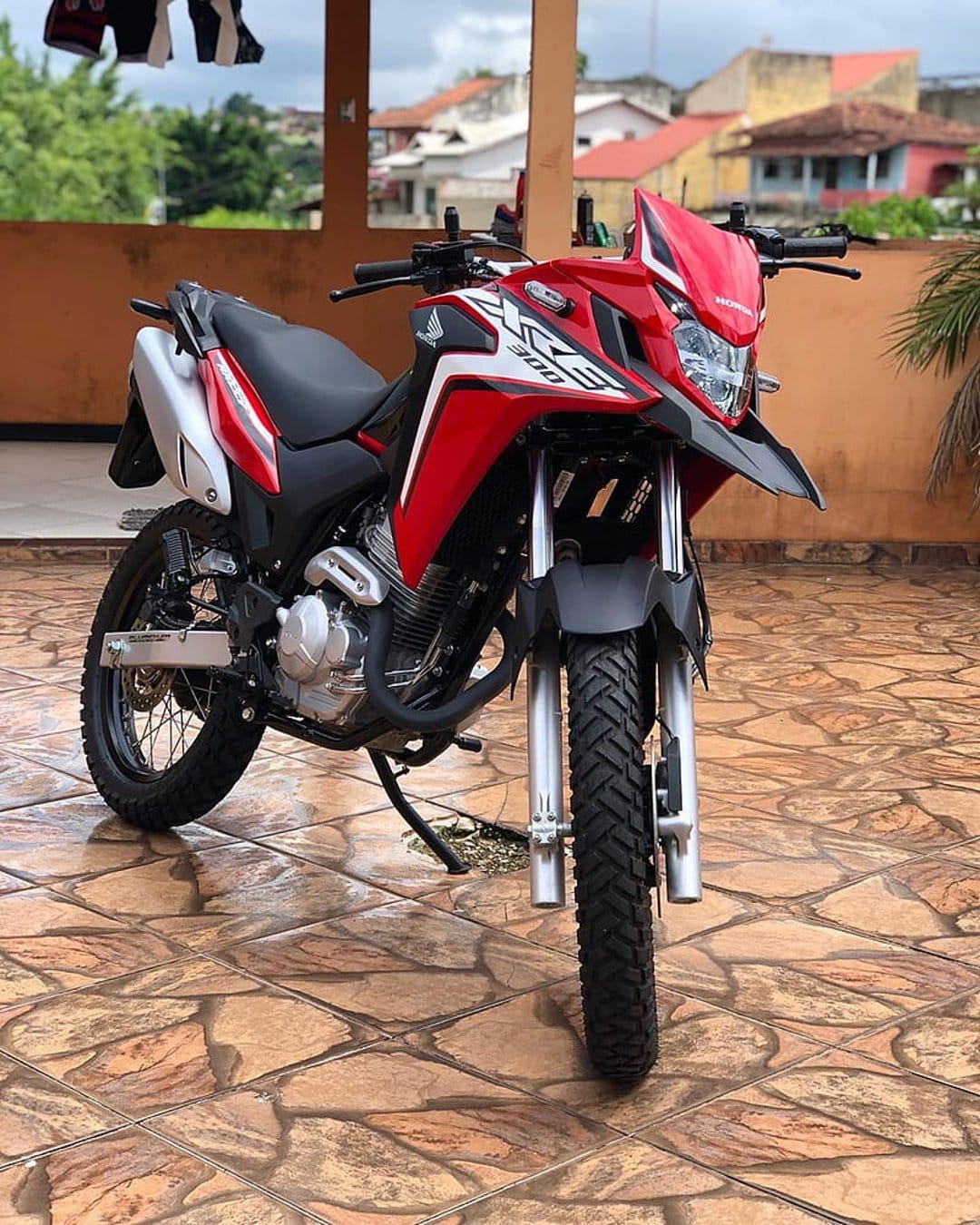 Red Honda XRE 300 motorcycle parked on a tiled terrace with visible front suspension and off-road tires.